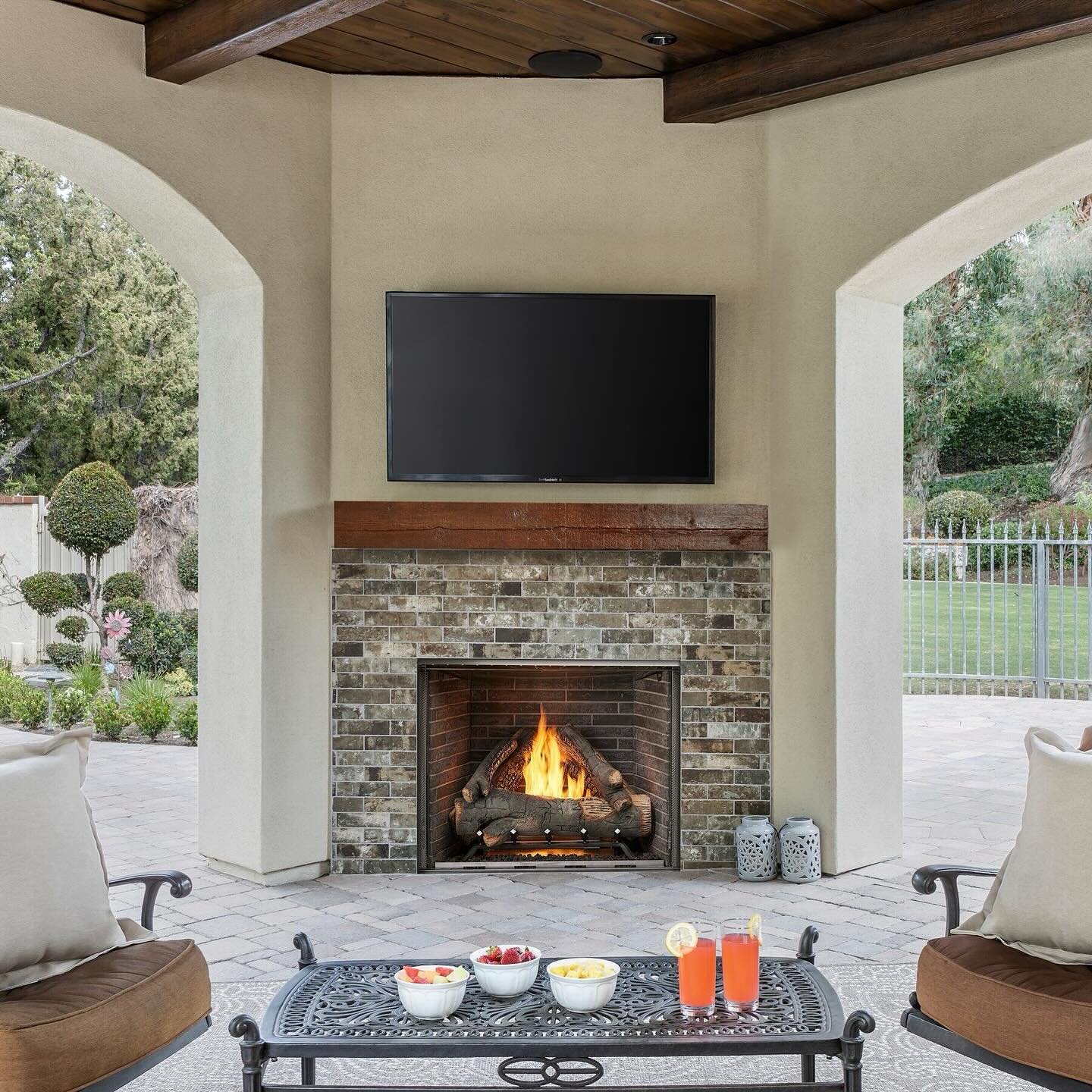 Traditional masonry fireplace with dark, varied brick and a wooden mantel, set into an arched patio wall.