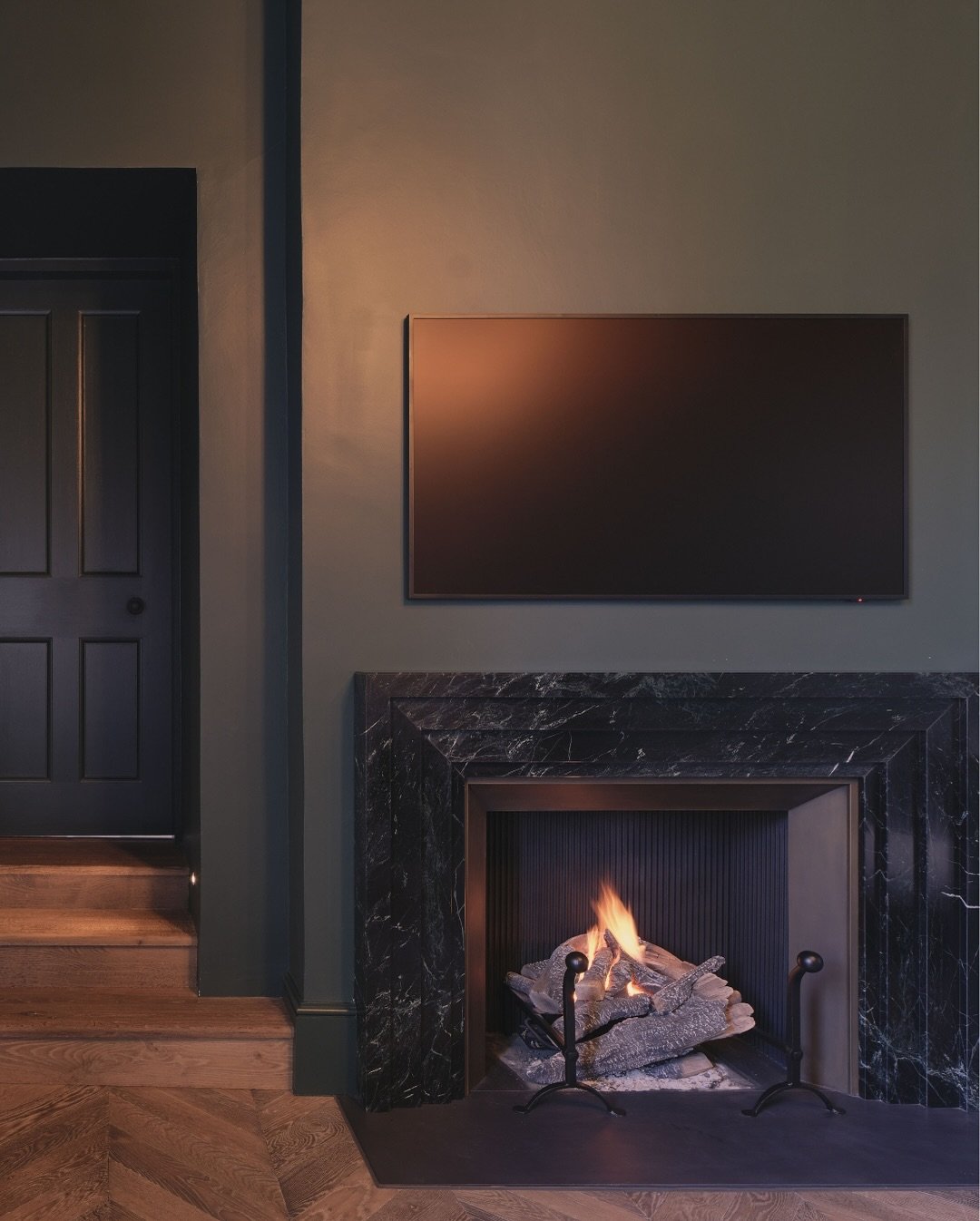 A fireplace surround crafted from deep black or dark green marble with white veining, set against a rich, matte olive green wall.