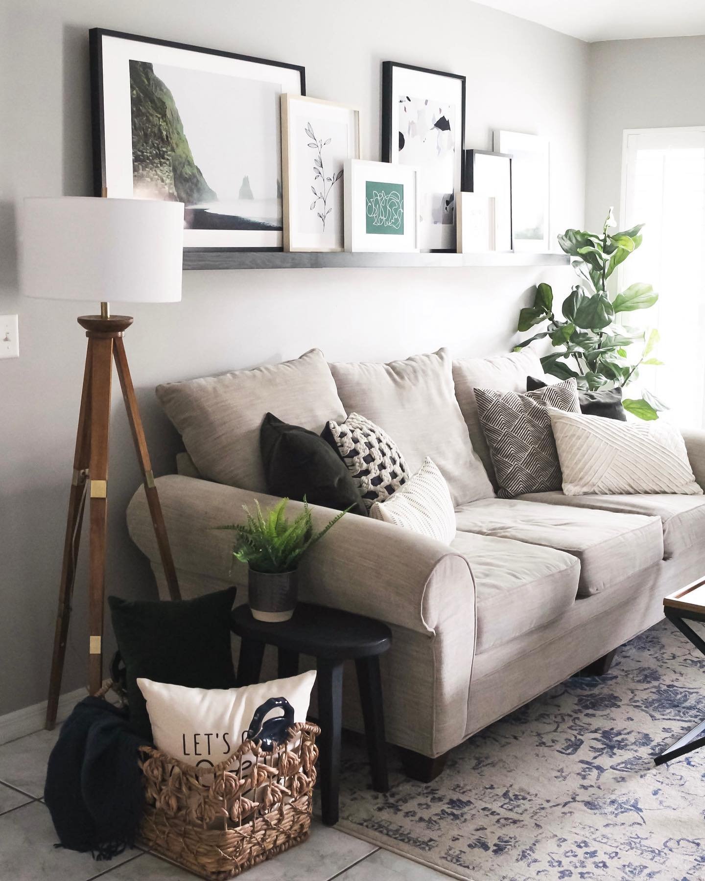 Dark gray picture ledge with overlapping framed art above a beige sofa with a tripod lamp