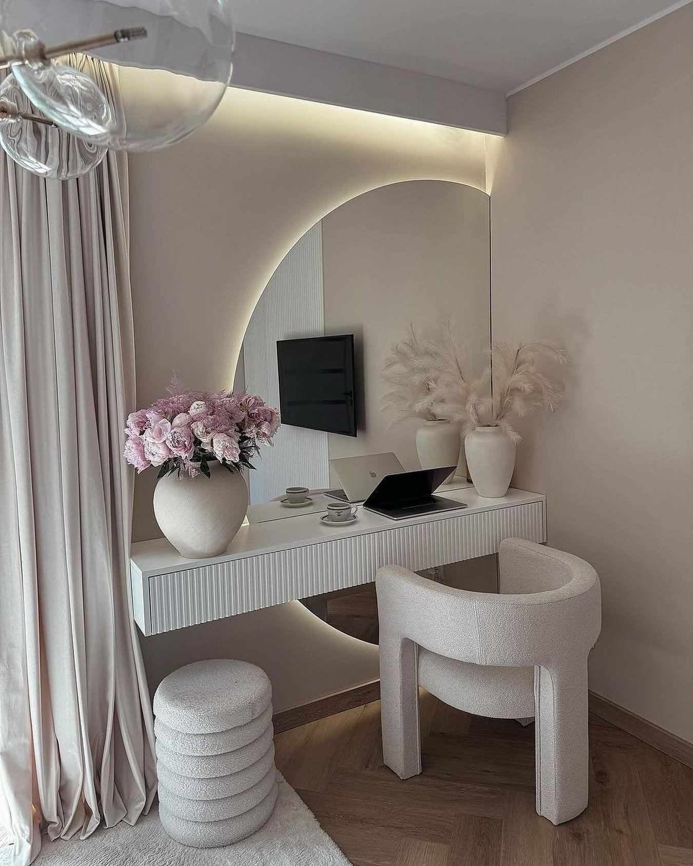 An ultra-modern white floating dressing table with fluted details, backed by a large arched mirror with perimeter lighting, and paired with a curved cream bouclé chair.
