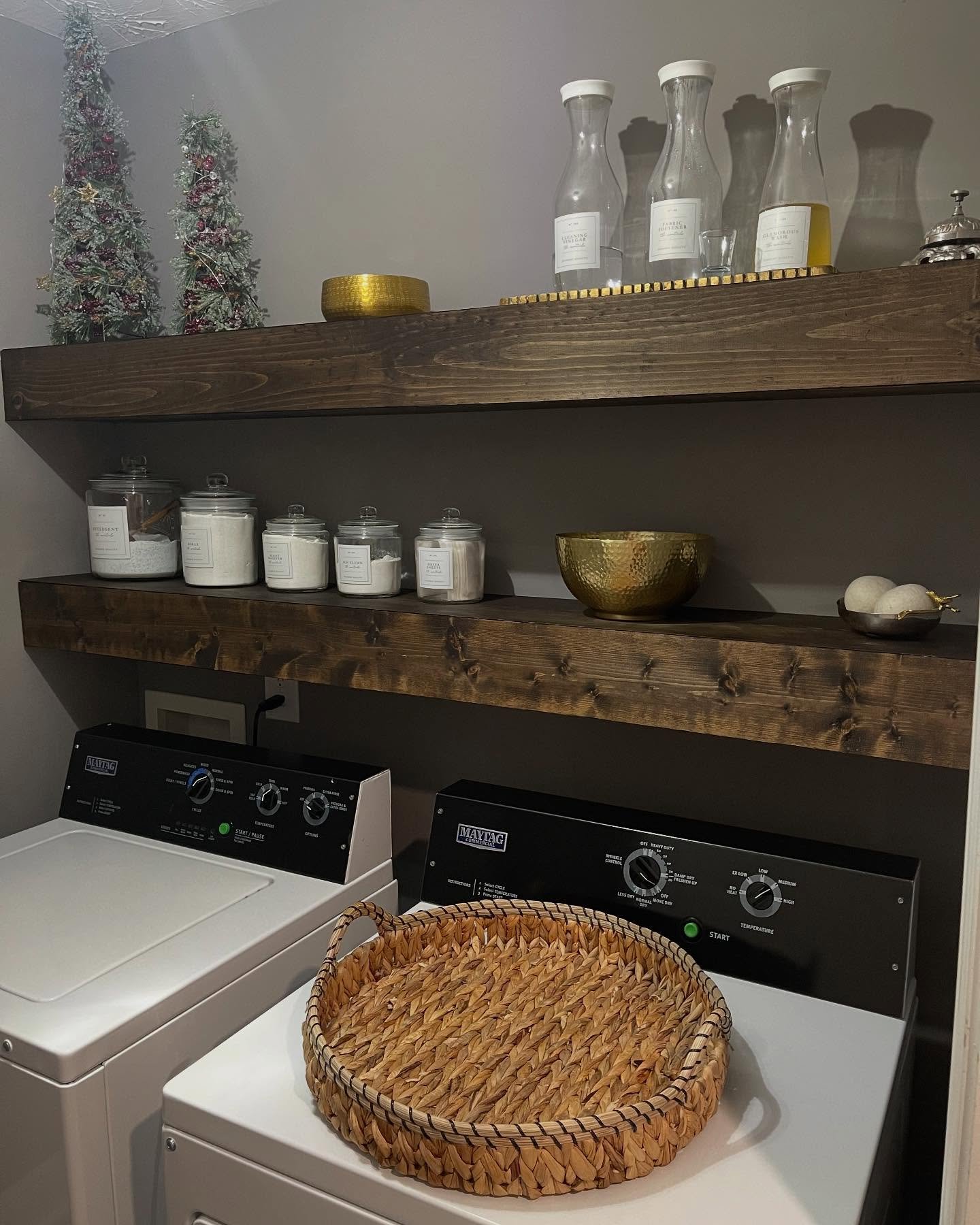 Thick dark stained wood laundry shelves holding glass jars and gold accents on a grey wall