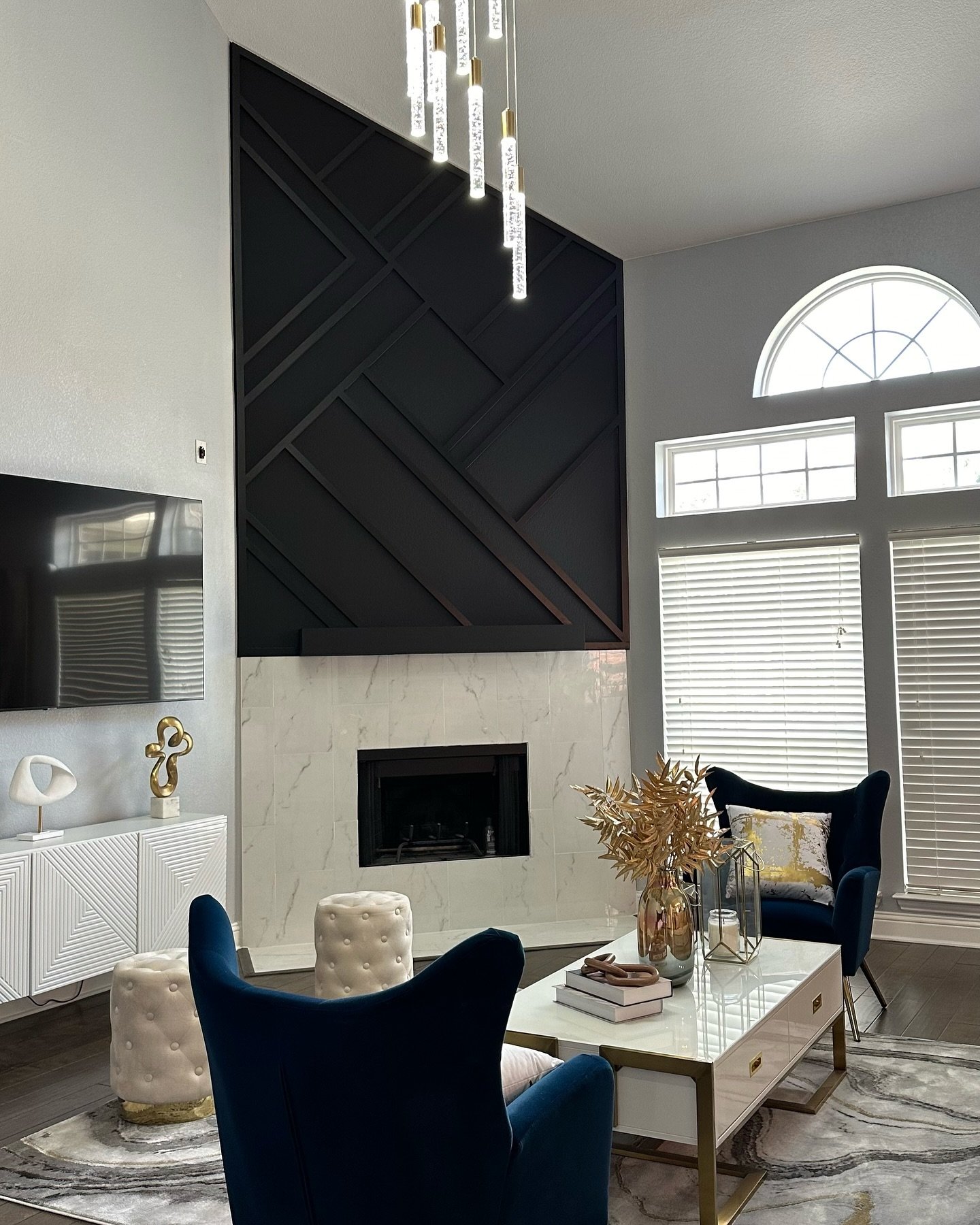 Modern living room featuring a tall, black geometric trim accent wall set above a square fireplace surrounded by white marble tile.