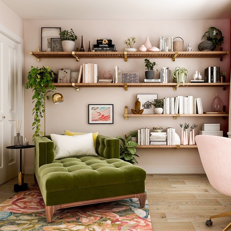 Modular wooden shelves with gold brackets filled with books and pink decor above a green velvet chaise