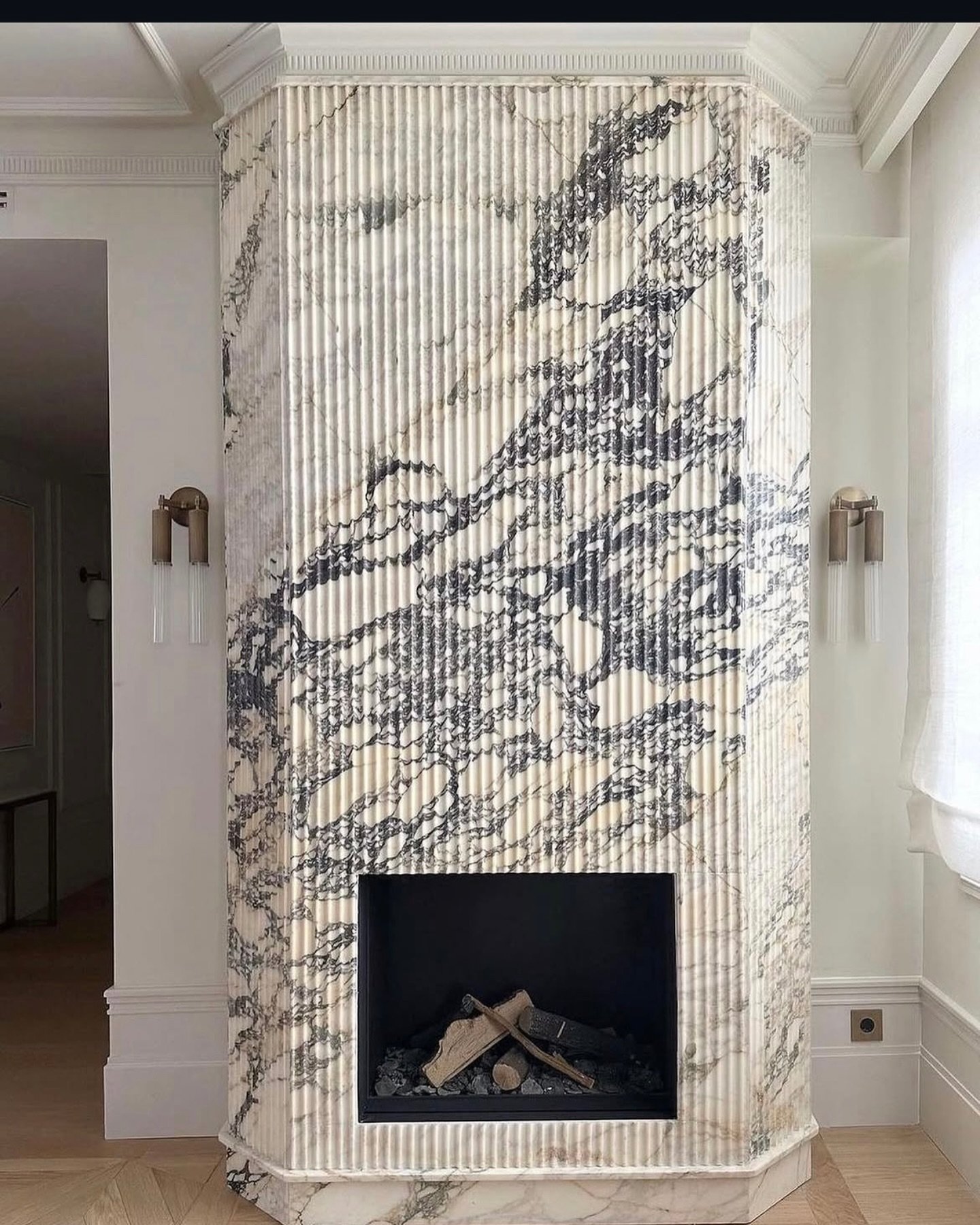 A striking floor-to-ceiling fireplace with a fluted, octagonal chimney breast covered in white marble with bold, dark grey veining.