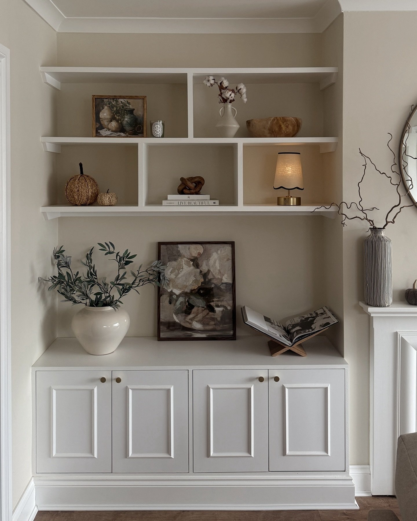 White built-in shelves with vertical dividers and paneled lower cabinets styled with art