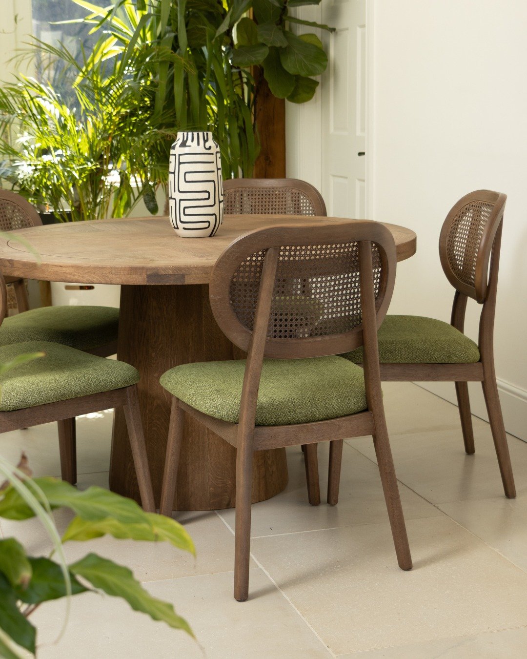 Round wooden pedestal dining table with cane back chairs and green seats