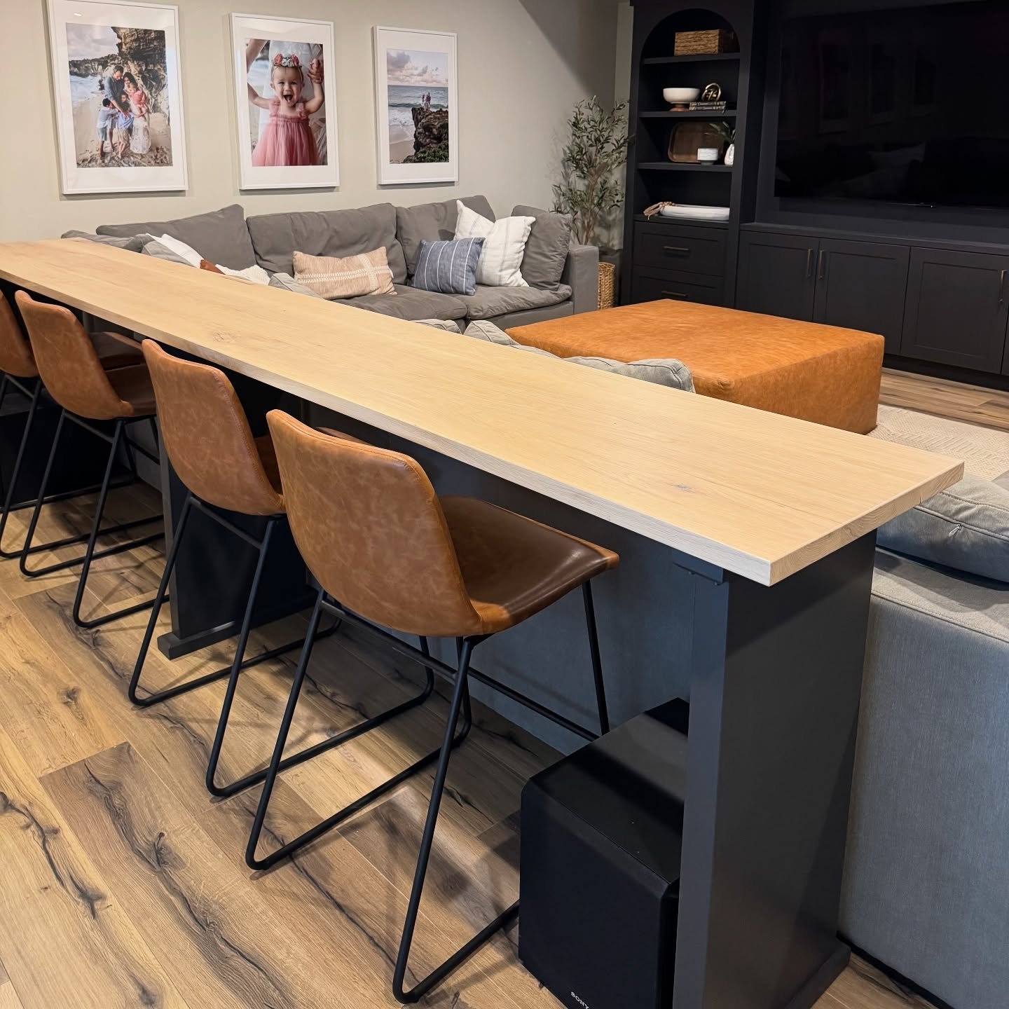 Long light wood bar table with brown leather stools behind grey sectional