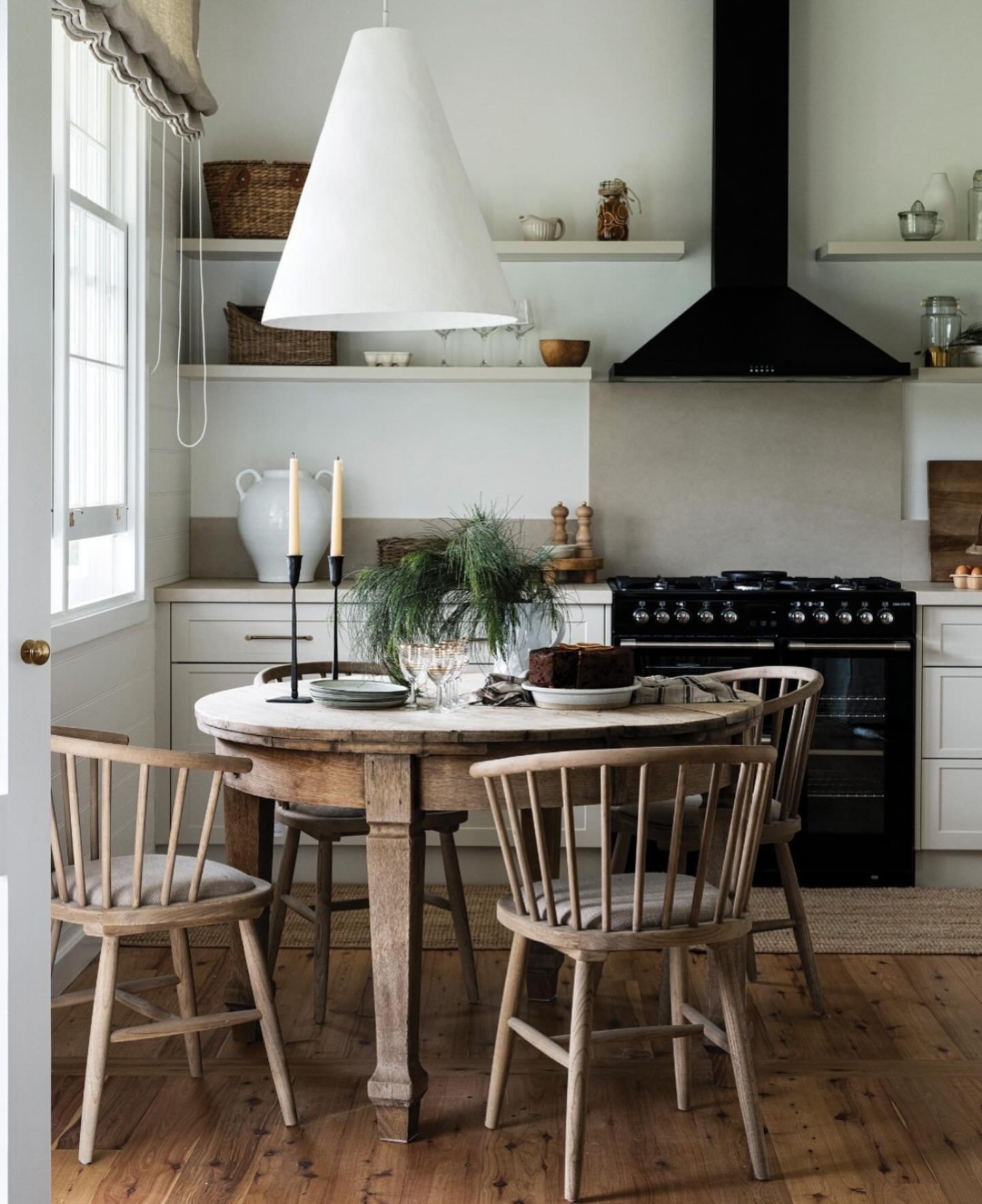 Round weathered wood dining table with spindle chairs in white kitchen