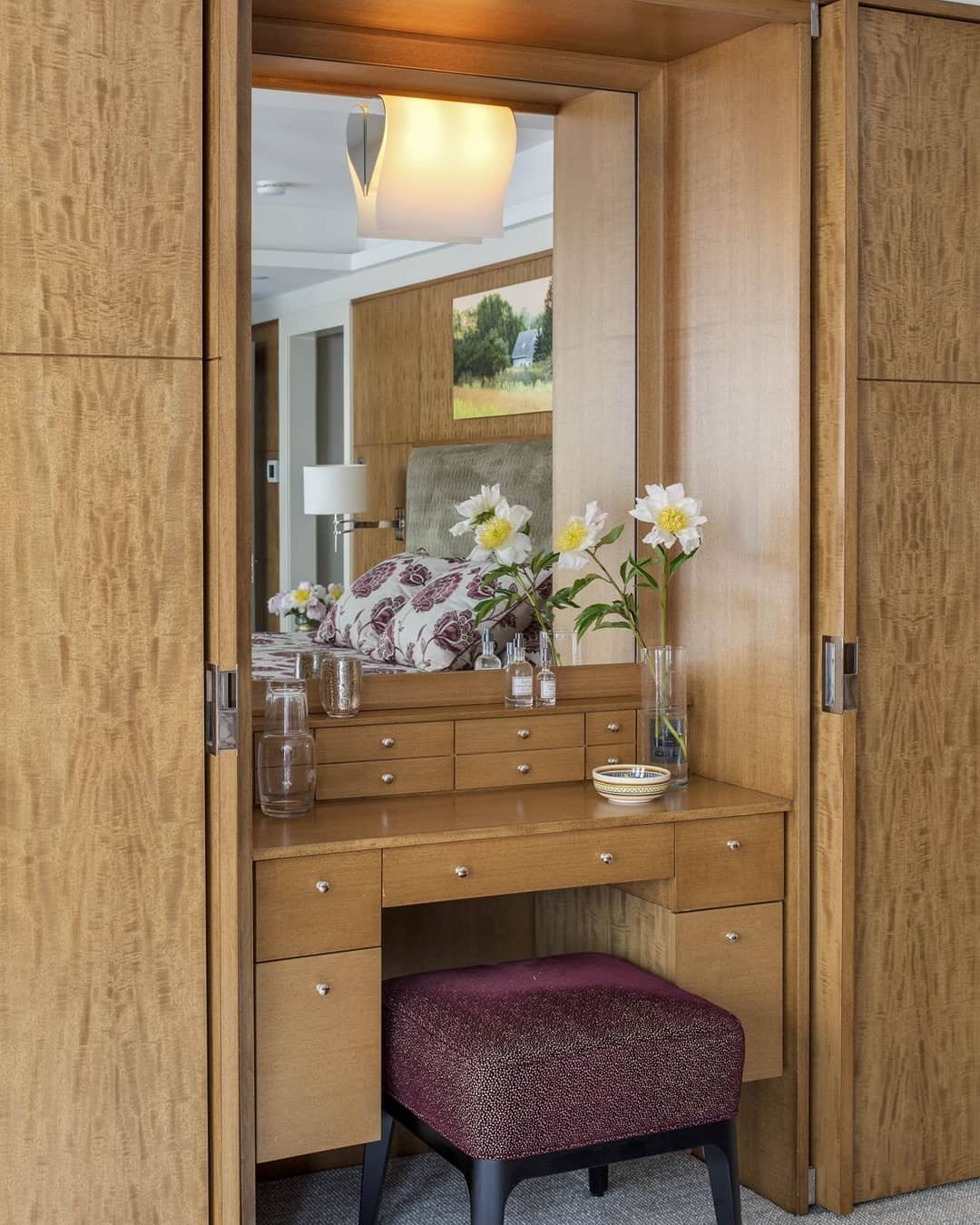 A compact dressing table finished in burl wood veneer, built into a wardrobe alcove with multiple small drawers, a large integrated mirror, and a deep purple fabric stool tucked beneath.