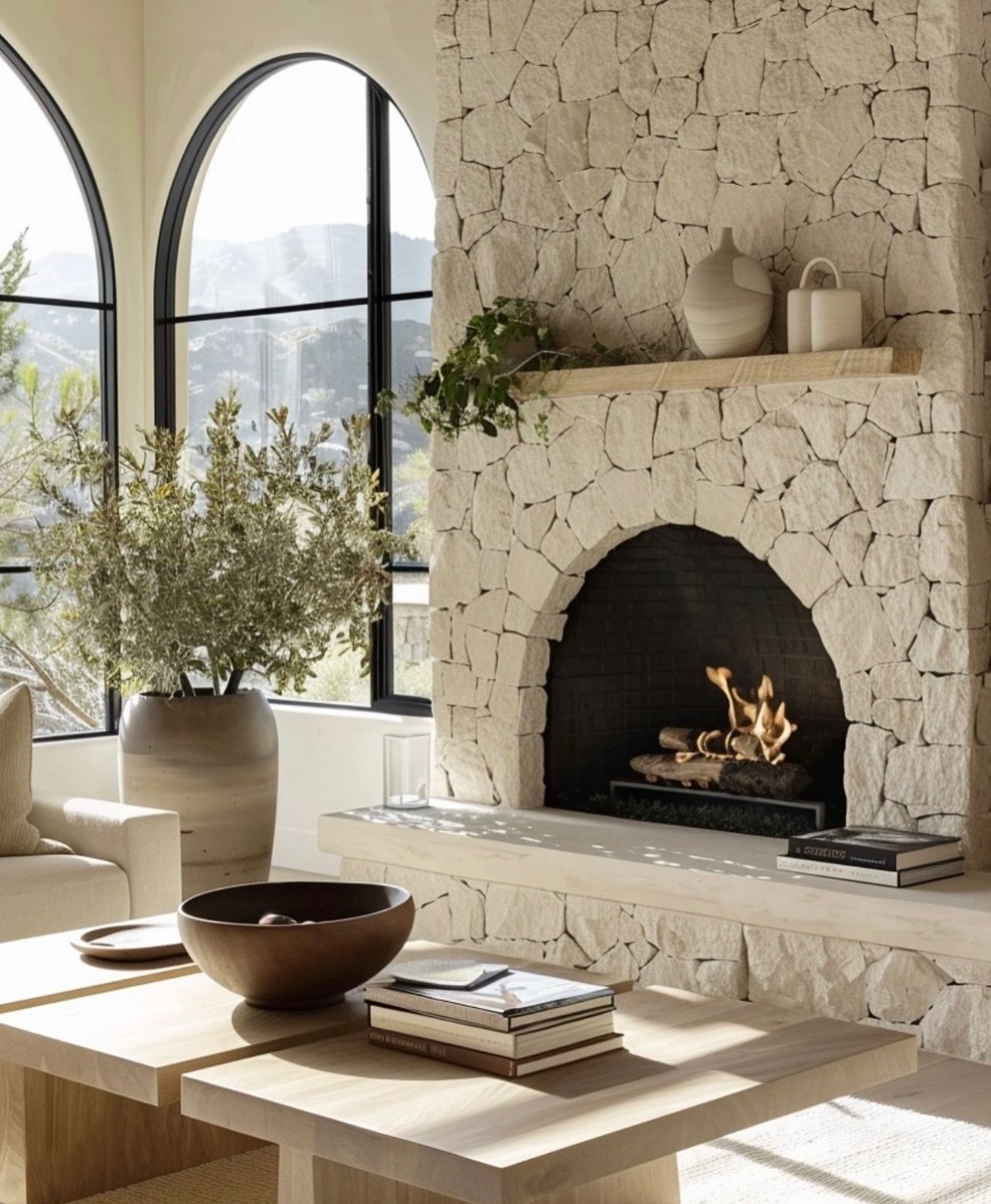 A wide, floor-to-ceiling fireplace constructed from light-colored, roughly cut stone, featuring a striking arched firebox opening and a smooth, thick stone hearth, set against a backdrop of arched windows.