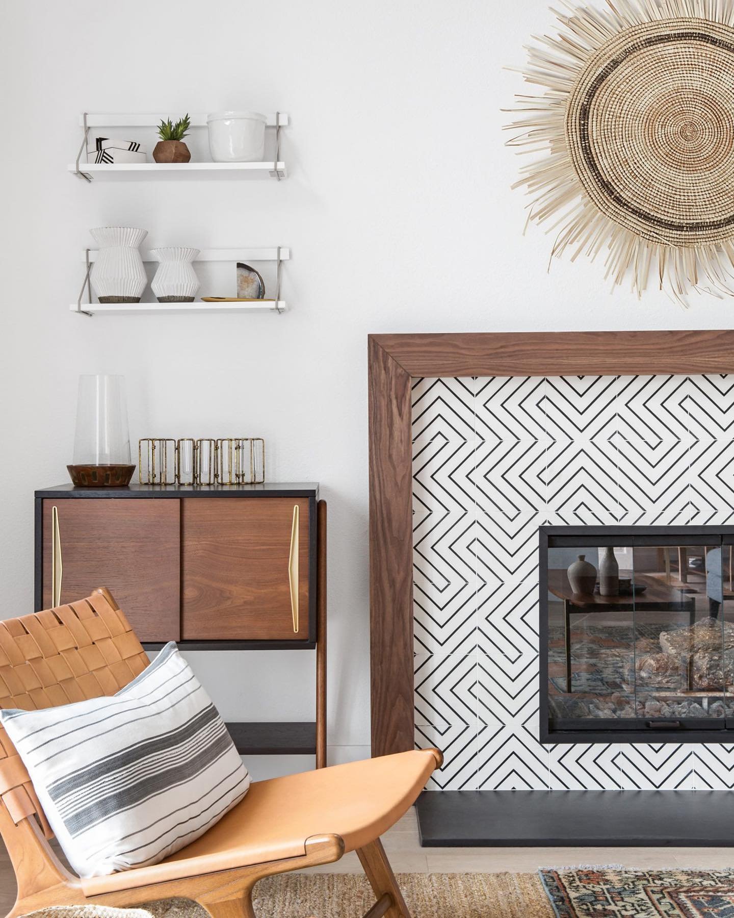 A modern fireplace featuring a thick walnut wood surround and large tiles with a black and white geometric maze-like pattern.