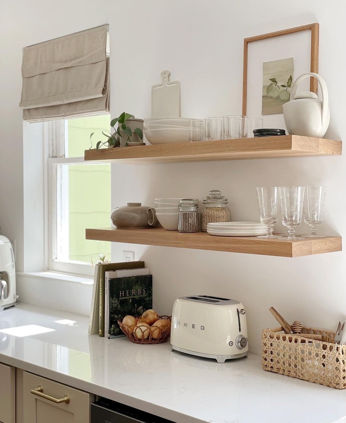 Two long, light wood floating shelves above a kitchen counter holding white dishes and glassware.