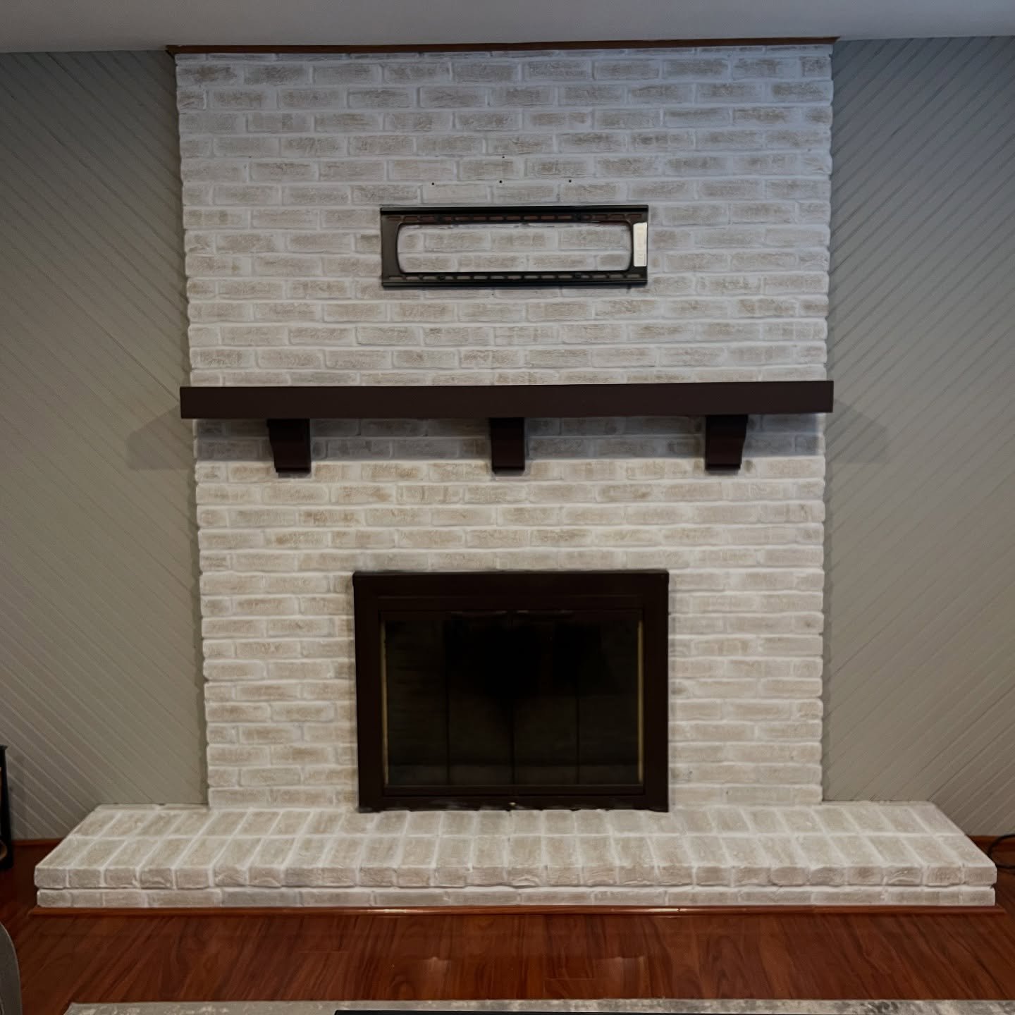 A tall brick fireplace treated with a German Schmear technique, giving it a heavily textured, off-white finish. It features a dark wood mantel and hearth.
