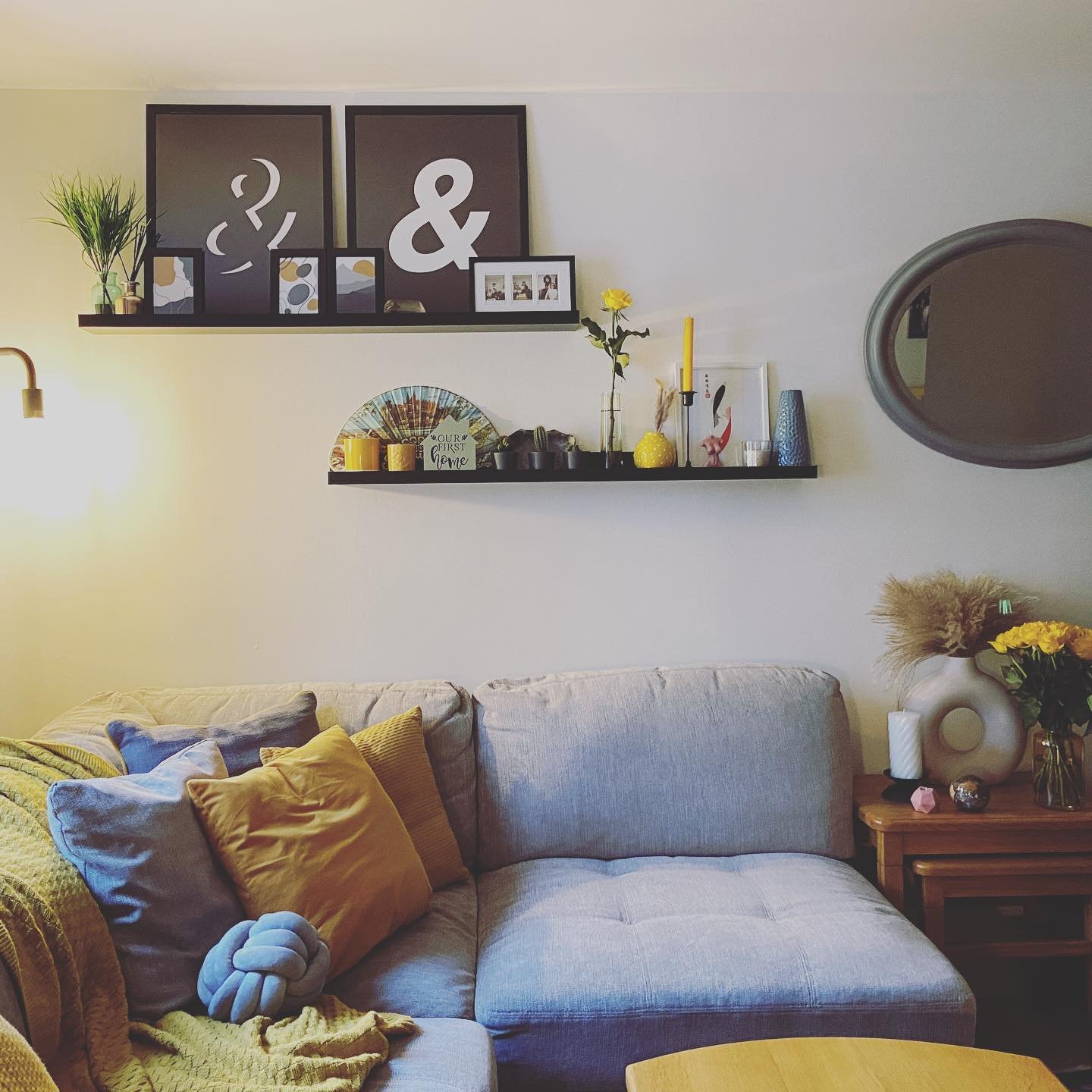 Staggered black shelves displaying yellow decor and typography art above a grey sofa