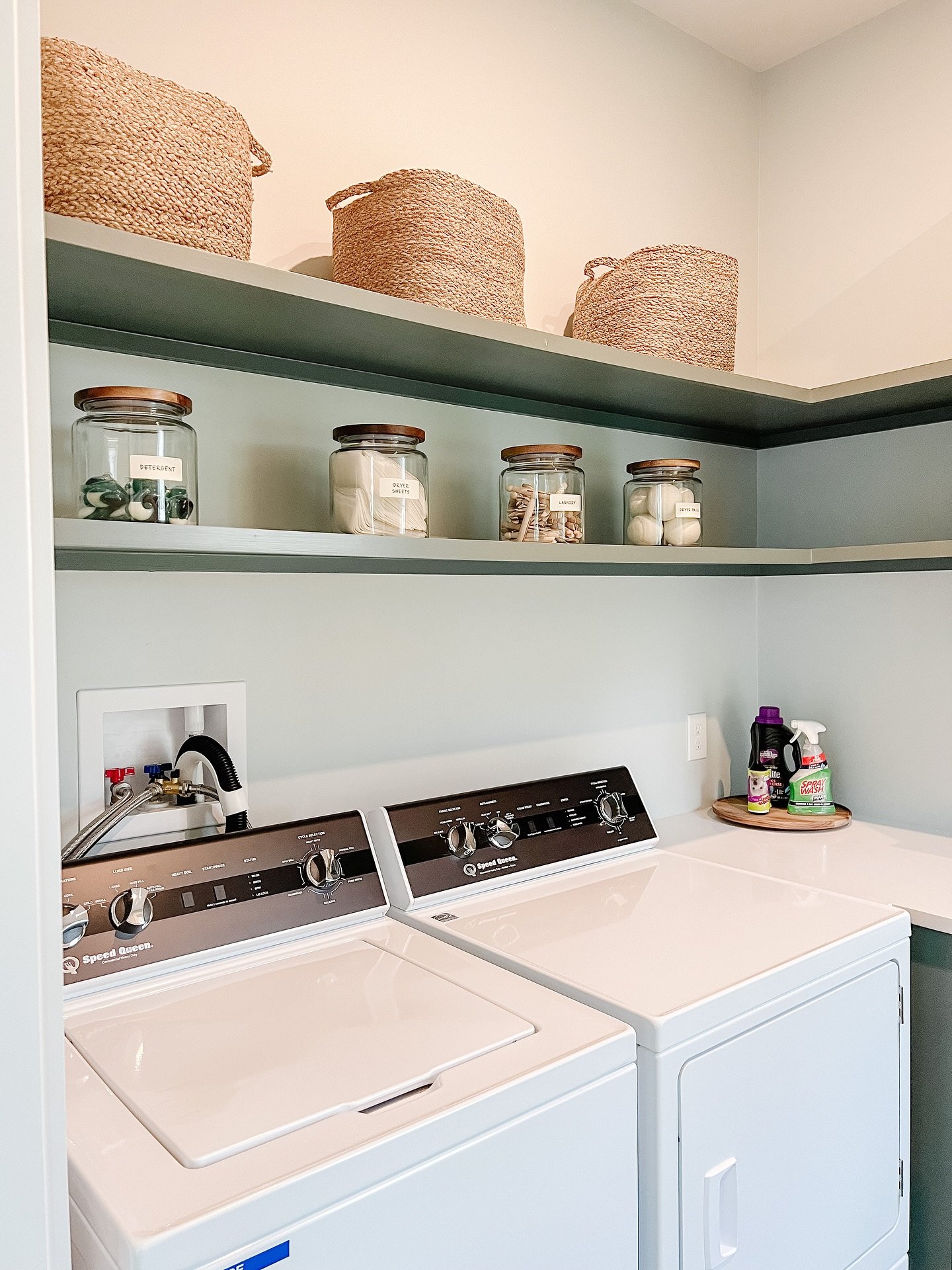 Sage green corner laundry shelves matching the wall color holding baskets and jars