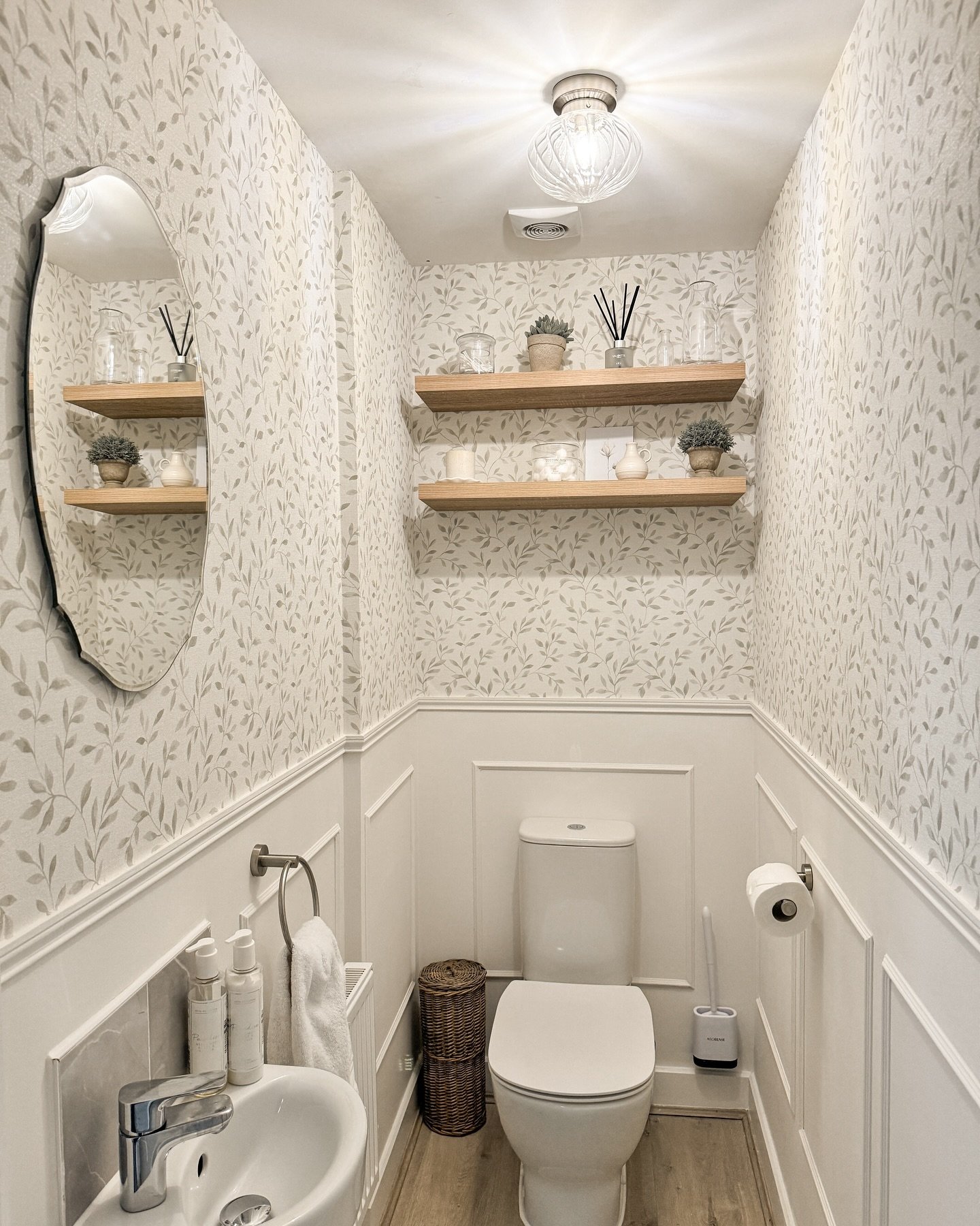 Two light wood floating shelves installed in a wallpapered bathroom alcove