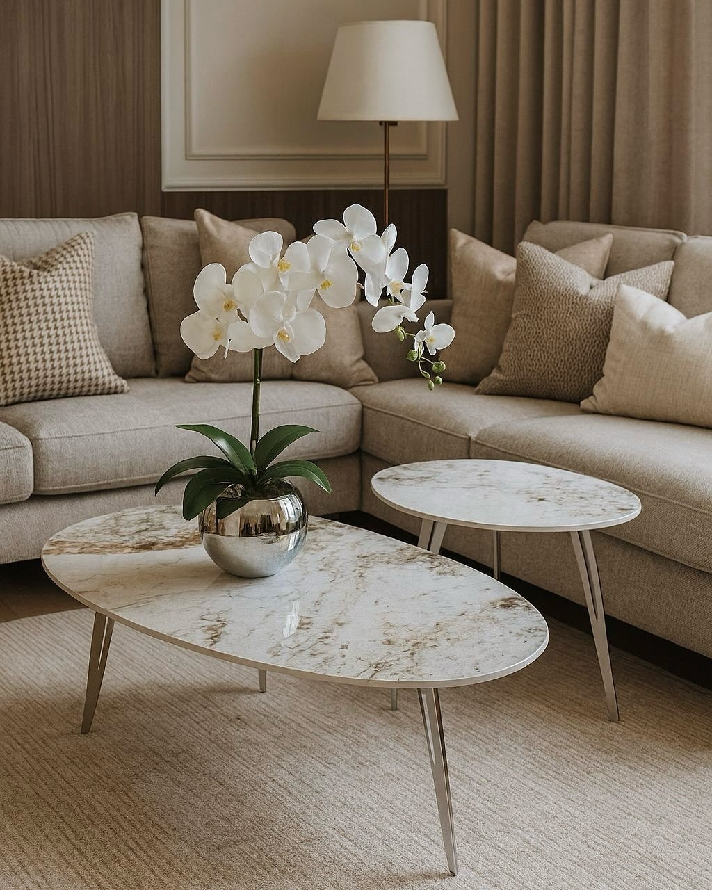 Two oval marble top coffee tables with silver legs in a beige living room