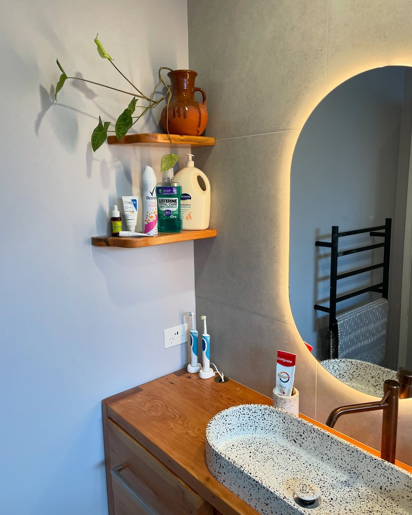 Two small, curved-front wooden floating shelves on a bathroom wall holding toiletries and a plant.