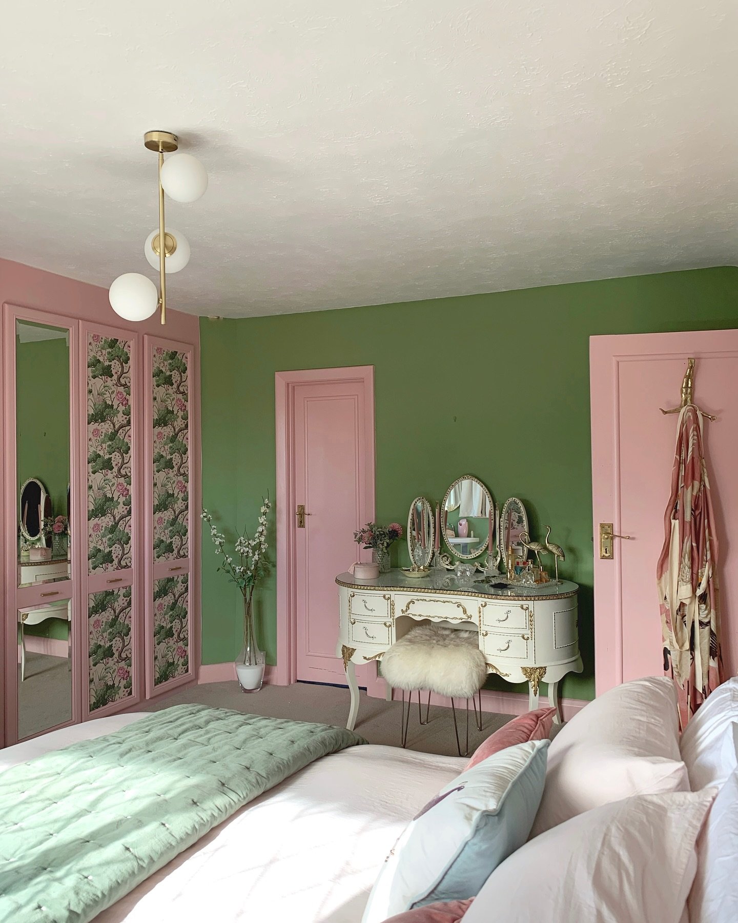 A colorful bedroom featuring solid block walls in bright green and doors painted in blush pink, a mirrored wardrobe with floral panels, and a vintage vanity.