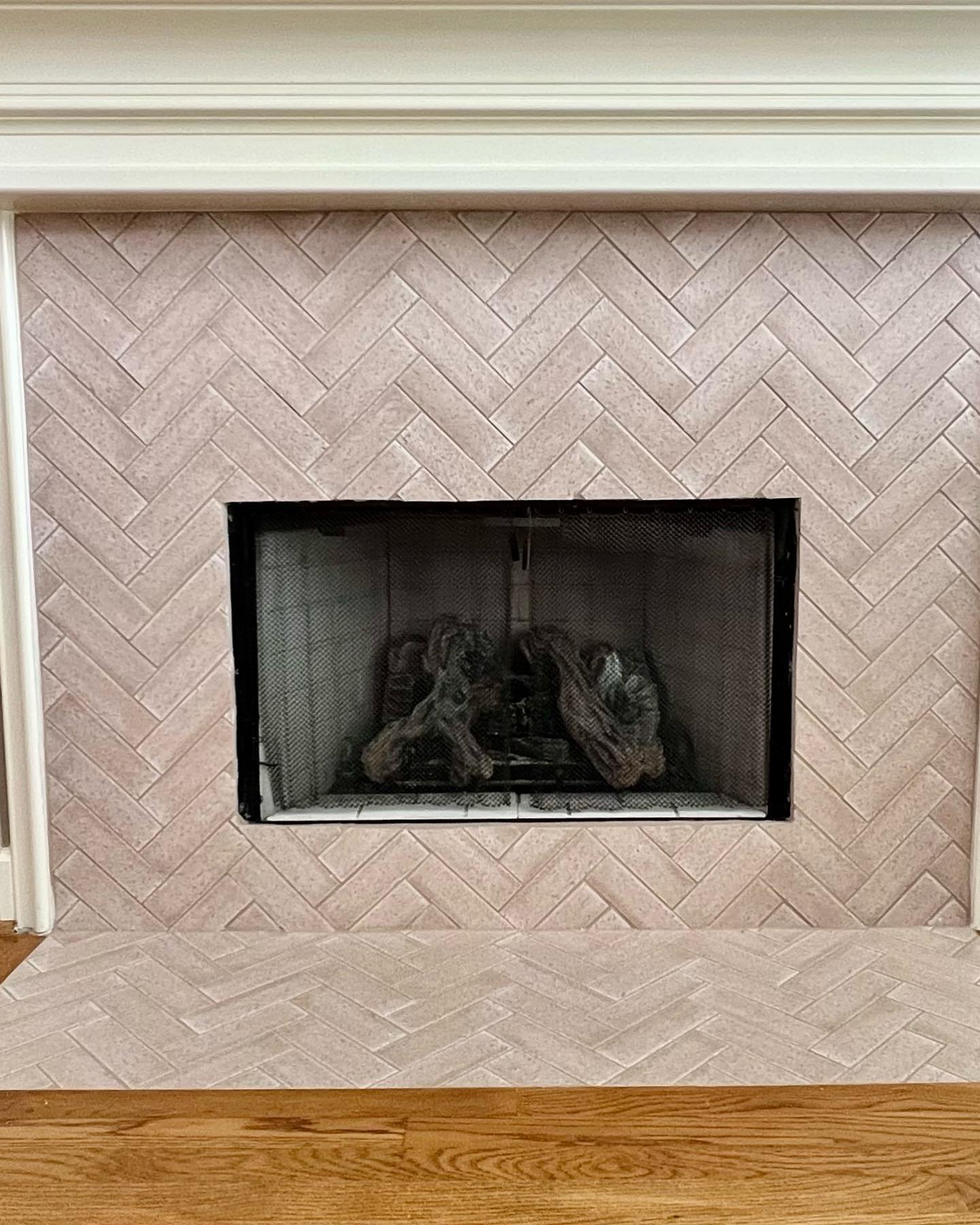A classic white fireplace featuring a surround and hearth tiled with rectangular pale pink ceramic tiles laid in a sophisticated chevron pattern.