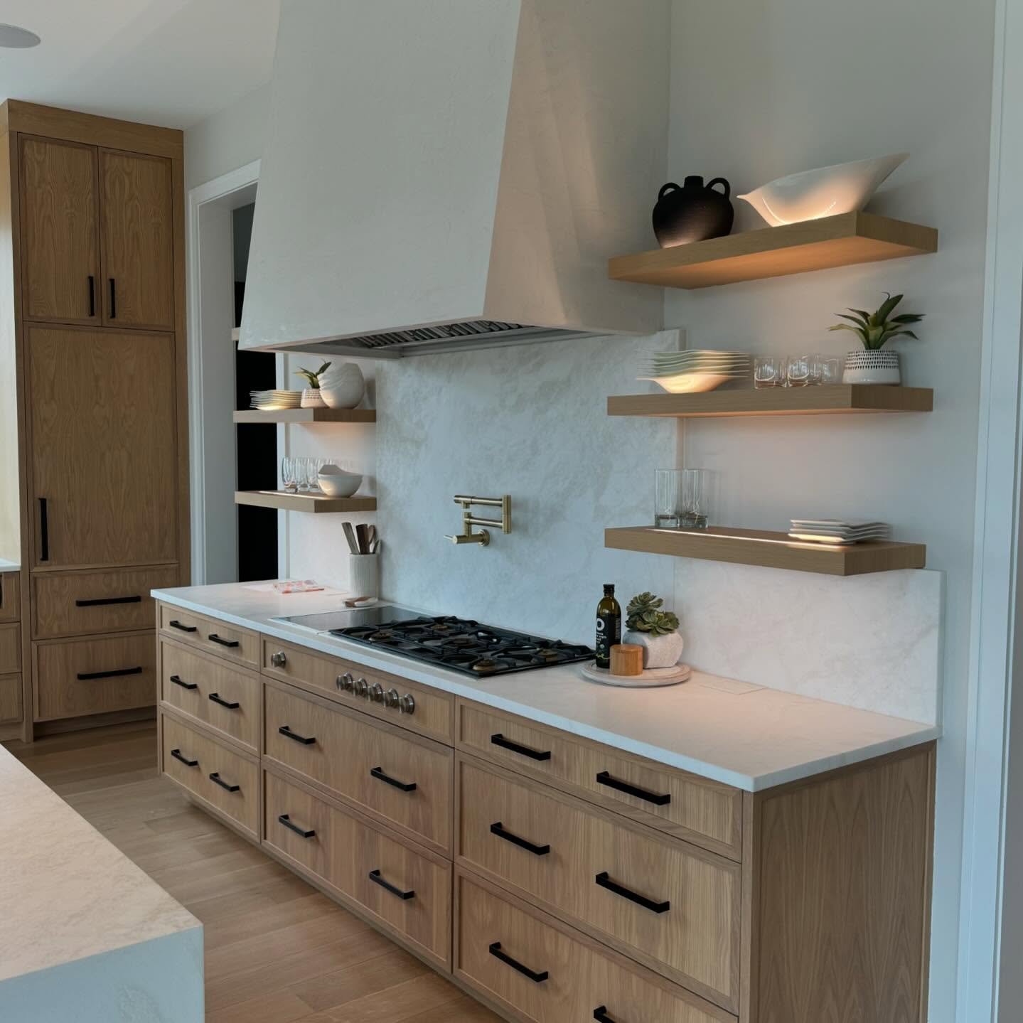 Light wood floating shelves with built-in lights on either side of a large modern range hood.