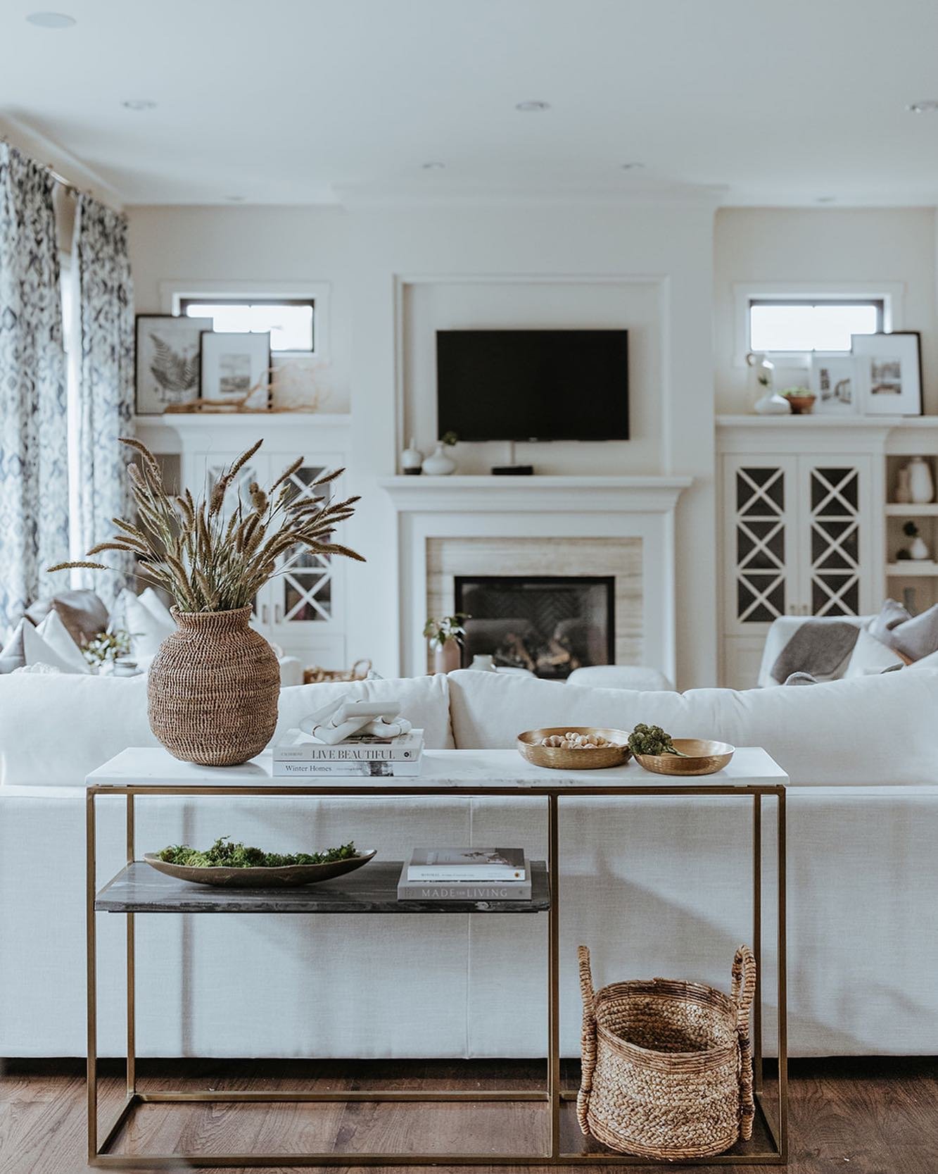 Slim gold console table with marble top styled with woven decor behind white sofa