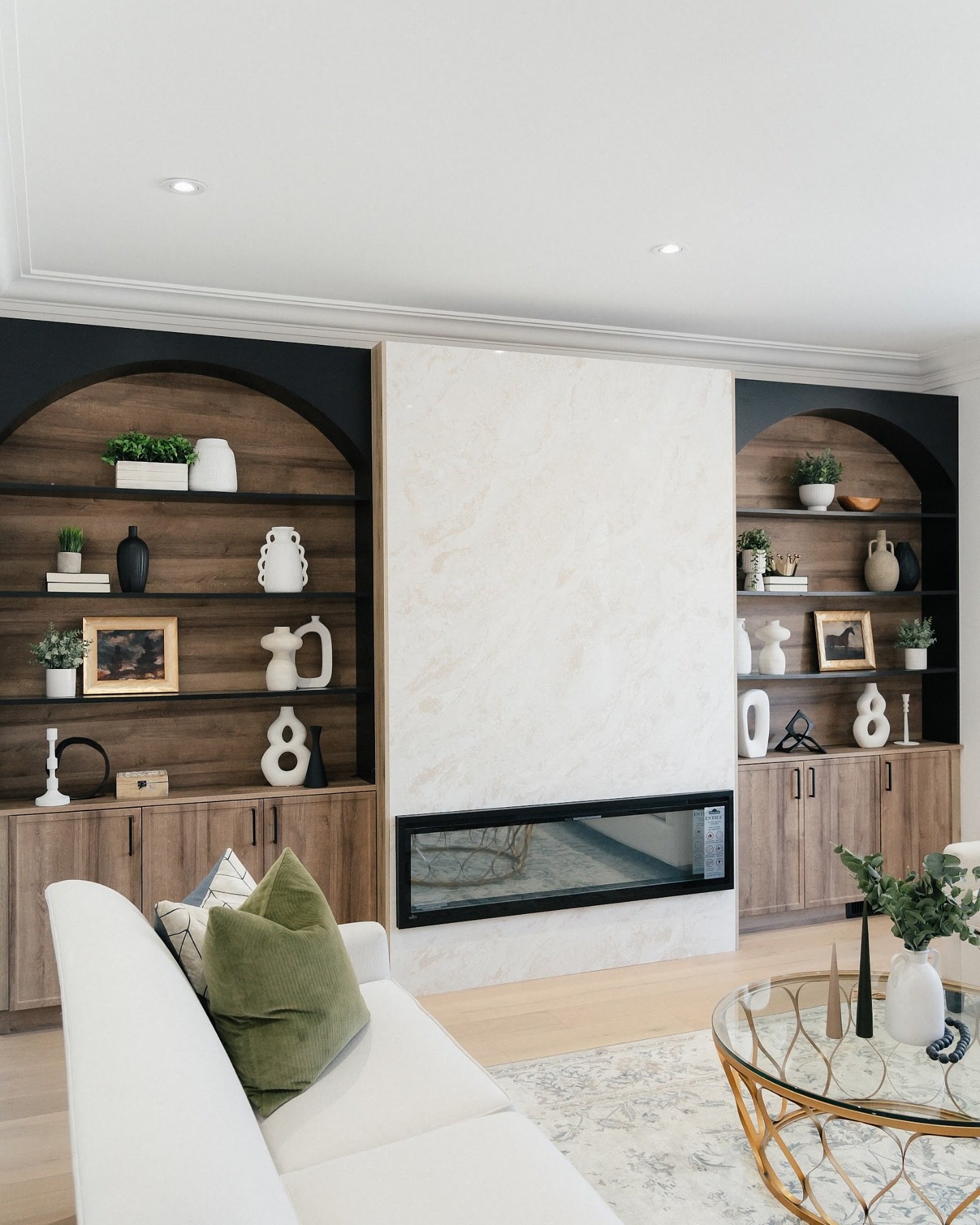 Black arched built-in shelves with wood backing flanking a marble fireplace wall.