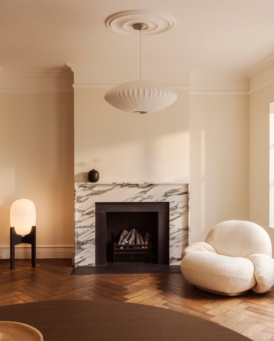 A white living room with a classic white marble fireplace surround featuring thick grey-black veining, complemented by rounded modern furniture and lighting.