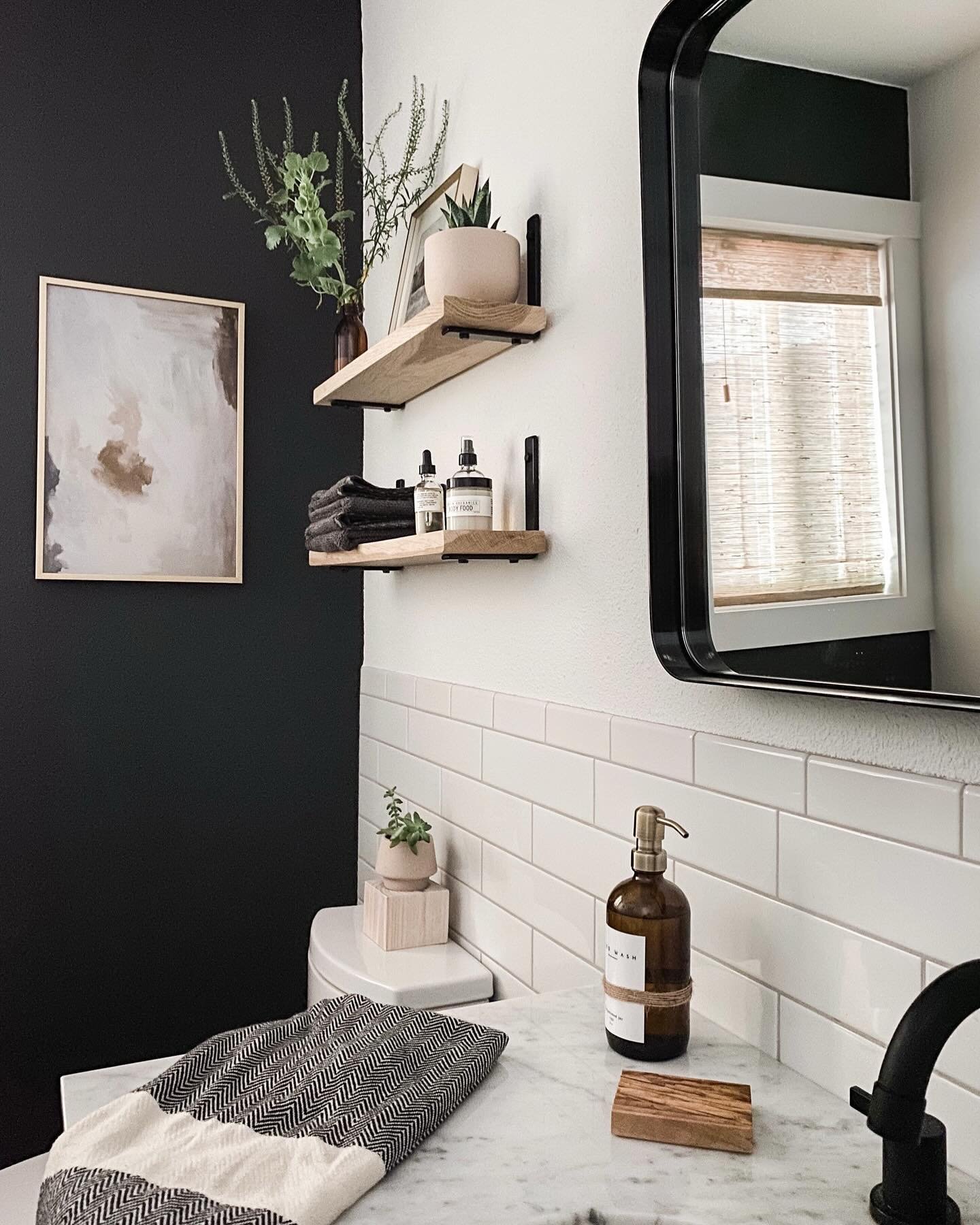 Two small light wood shelves with black brackets mounted on a white bathroom wall