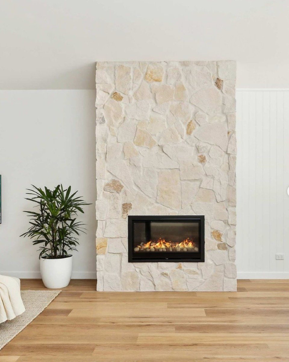 Minimalist living room with a floor-to-ceiling fireplace accent wall covered in light, irregular natural fieldstone with warm tan flecks.