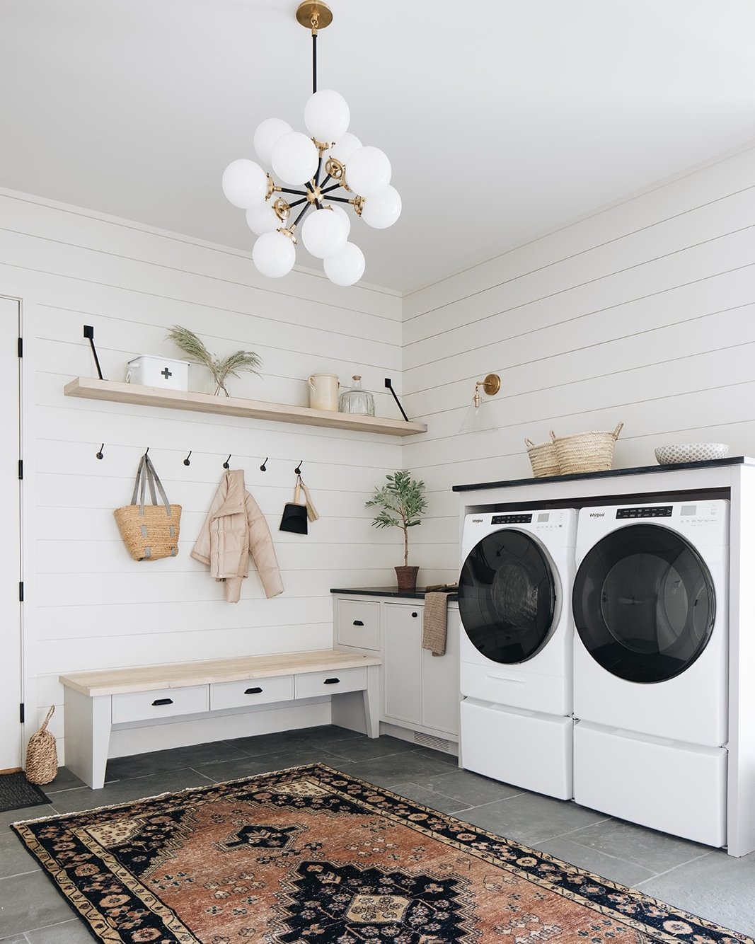 Light wood floating laundry shelf with black supports on white shiplap wall above coat hooks