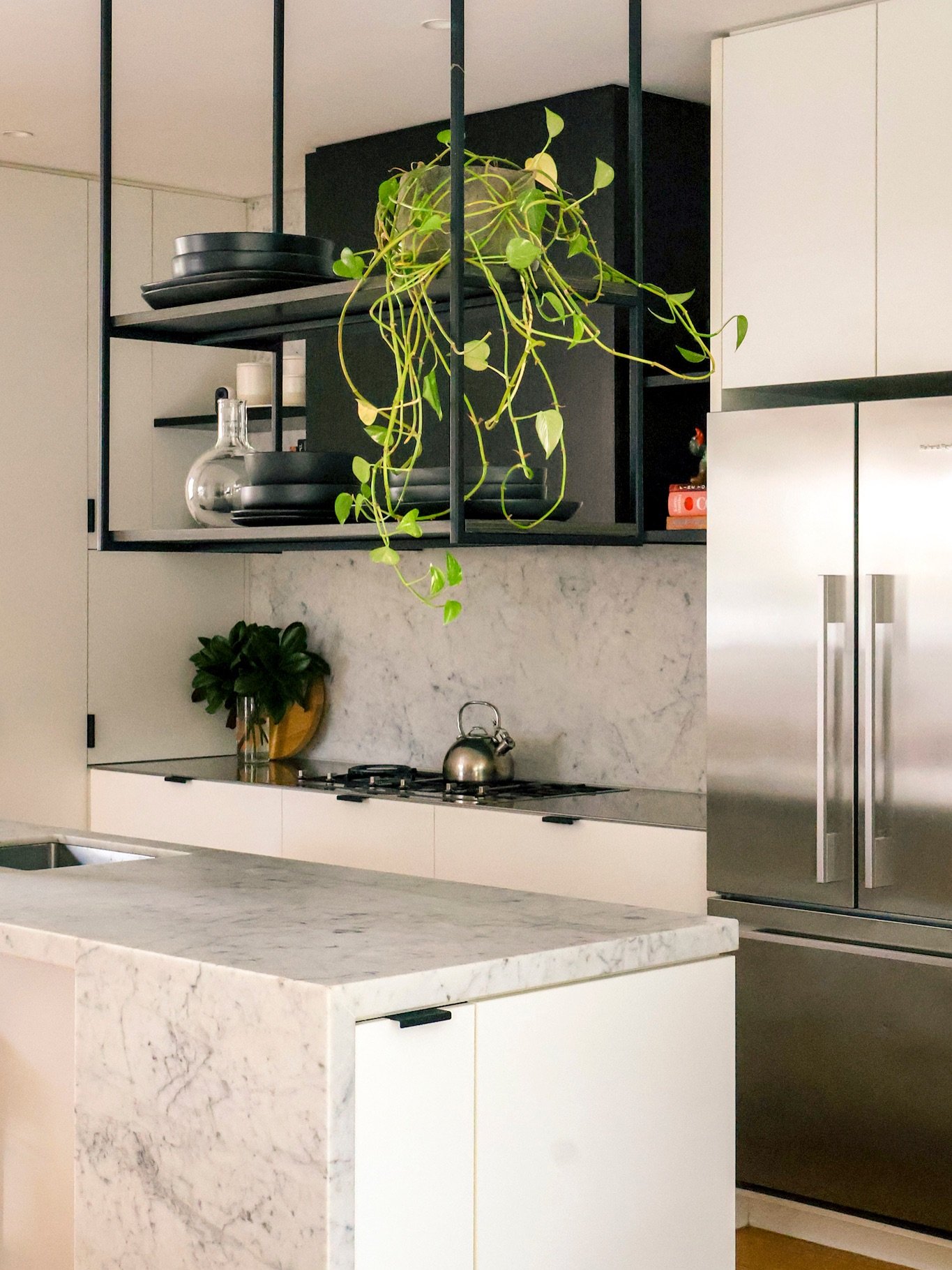 Black metal hanging shelves suspended from the ceiling over a kitchen counter, holding black dishes.