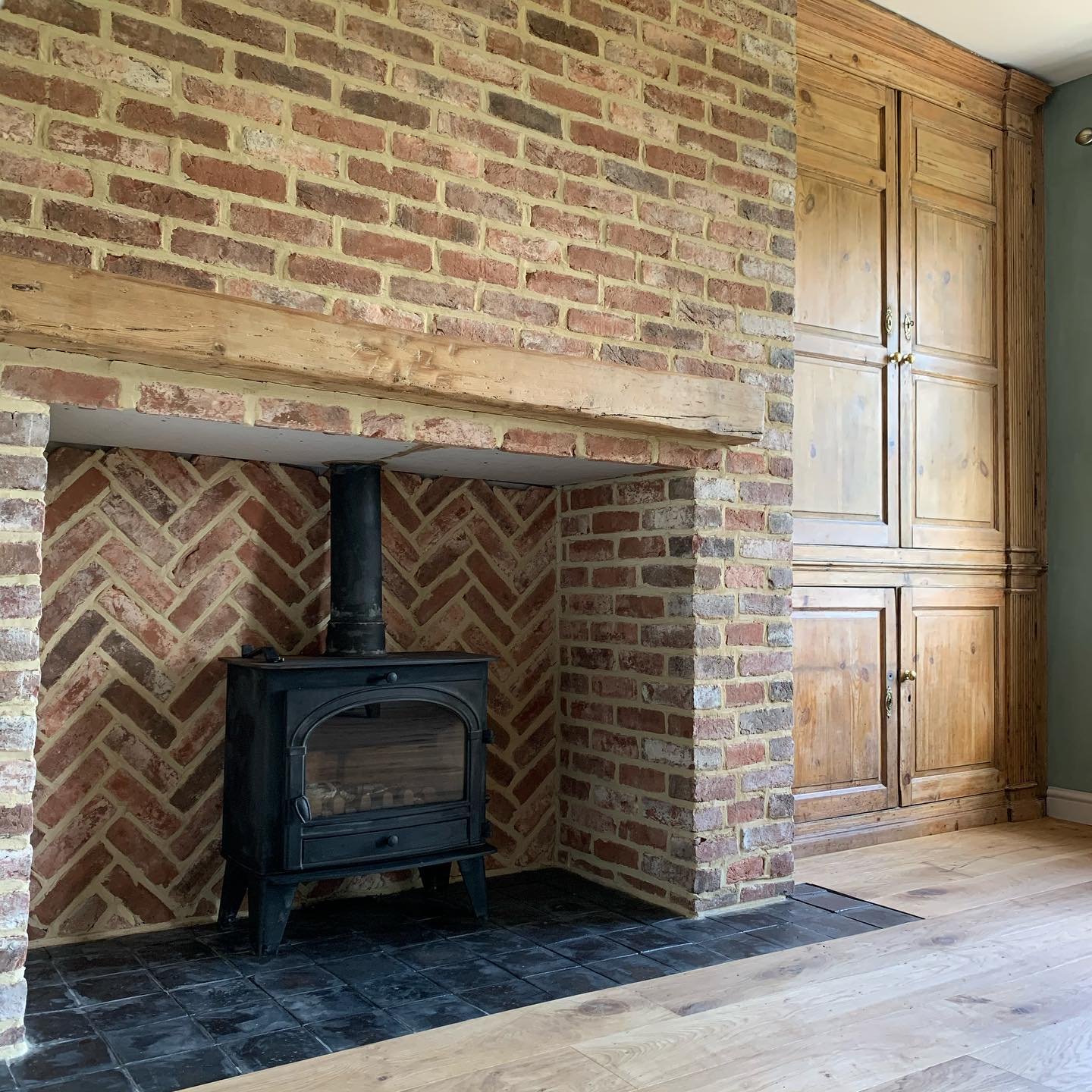 A rustic brick fireplace with a wood-burning stove. The exterior brick is laid in a running bond, while the firebox interior uses a herringbone pattern.