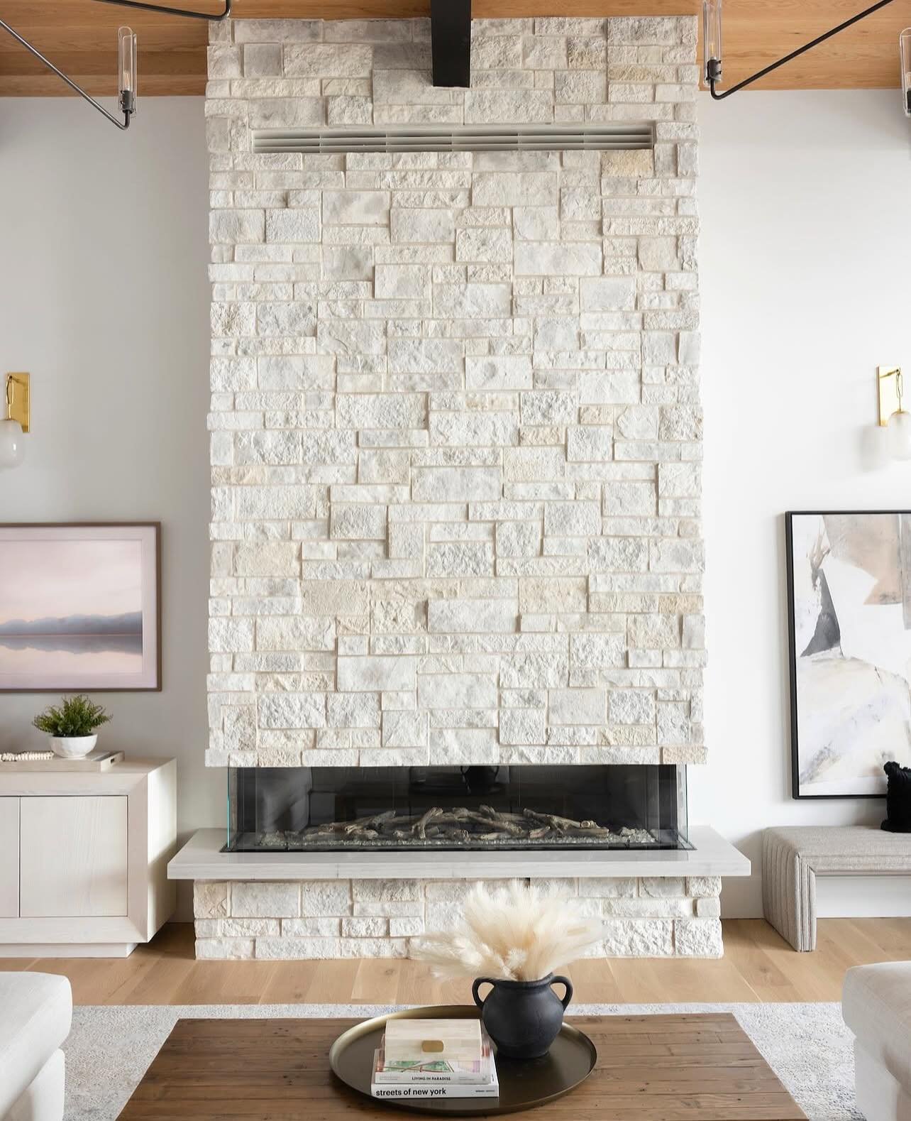 A massive, full-height rectangular stone fireplace wall made of white and pale grey rectangular-cut stone, featuring a wide, glass-enclosed linear gas firebox and minimal décor.