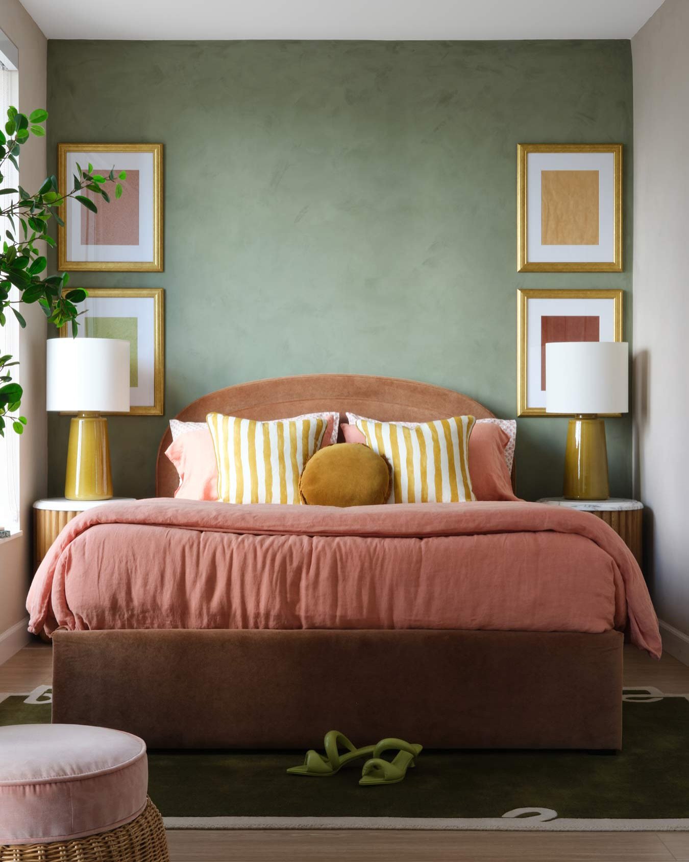 A bedroom featuring a moss green textured wall, a curved pink headboard, a large terracotta pink linen duvet, and matching yellow accents.