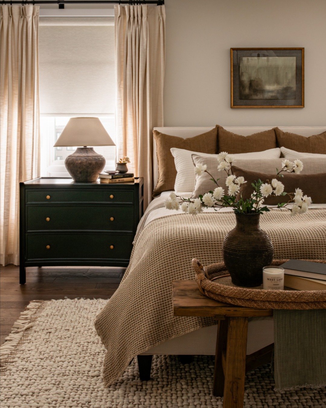 Bedroom with beige drapes, dark green nightstand, waffle bedding, and rustic wooden bench