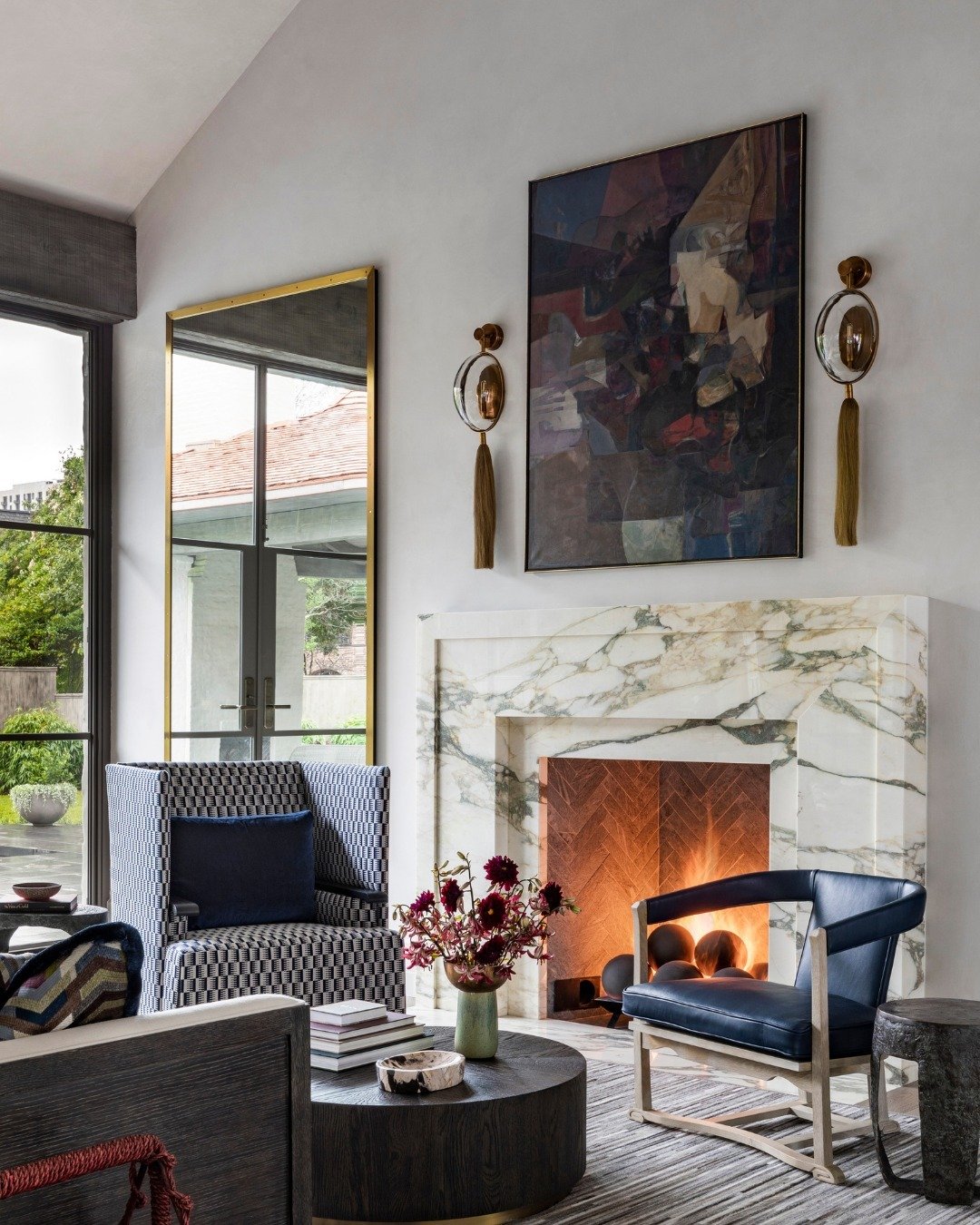 An artistic living space featuring a white marble fireplace with thick gold and grey veining, a brick herringbone firebox interior, and eclectic furnishings.