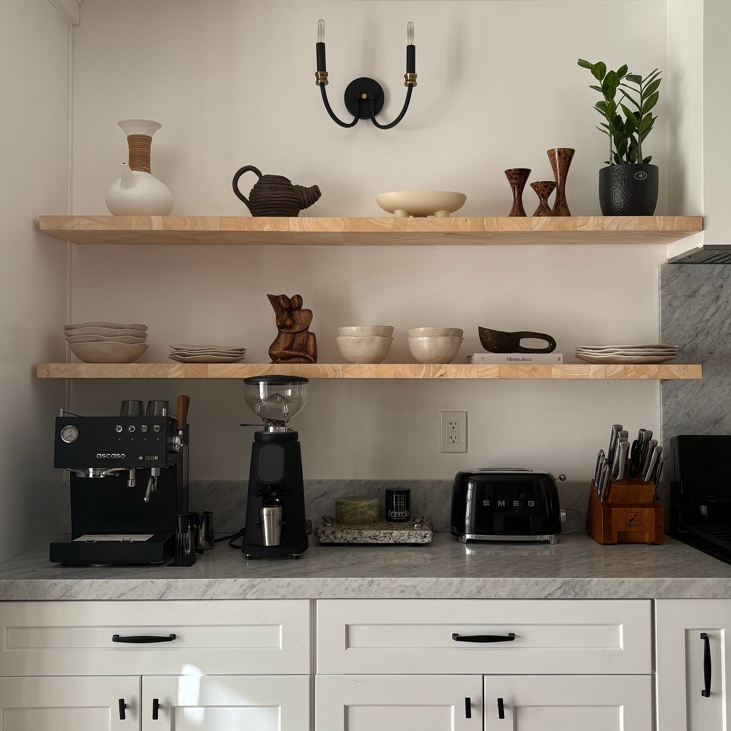 Two long, light wood floating shelves above a coffee bar, styled with artistic pottery and ceramics.
