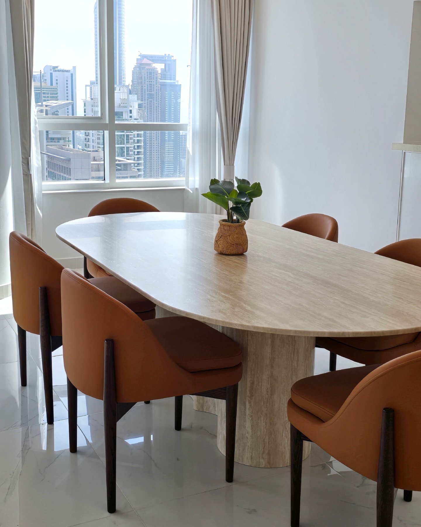 Oval travertine dining table with burnt orange chairs and city skyline view