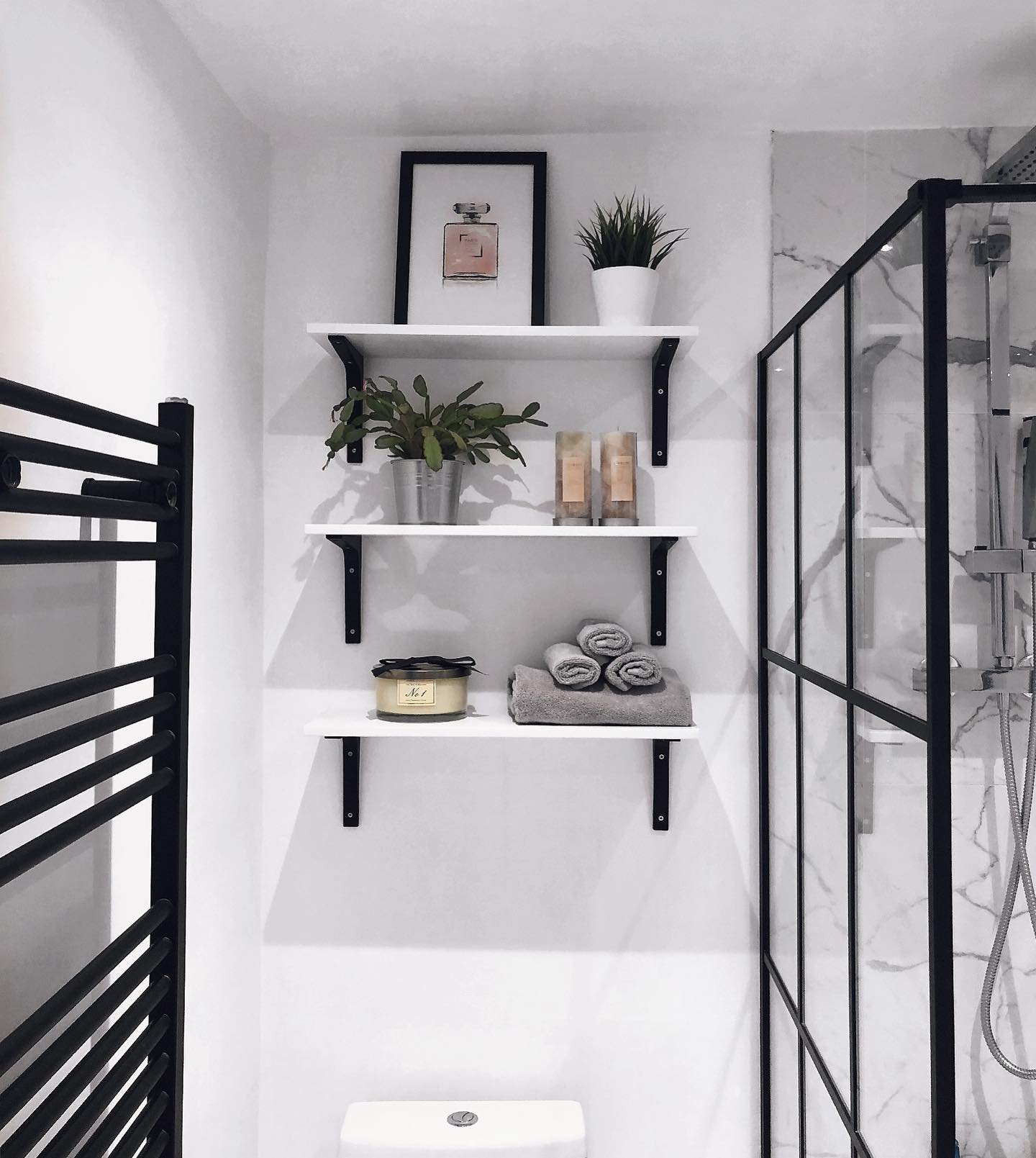 Three white shelves with black metal brackets arranged above a toilet