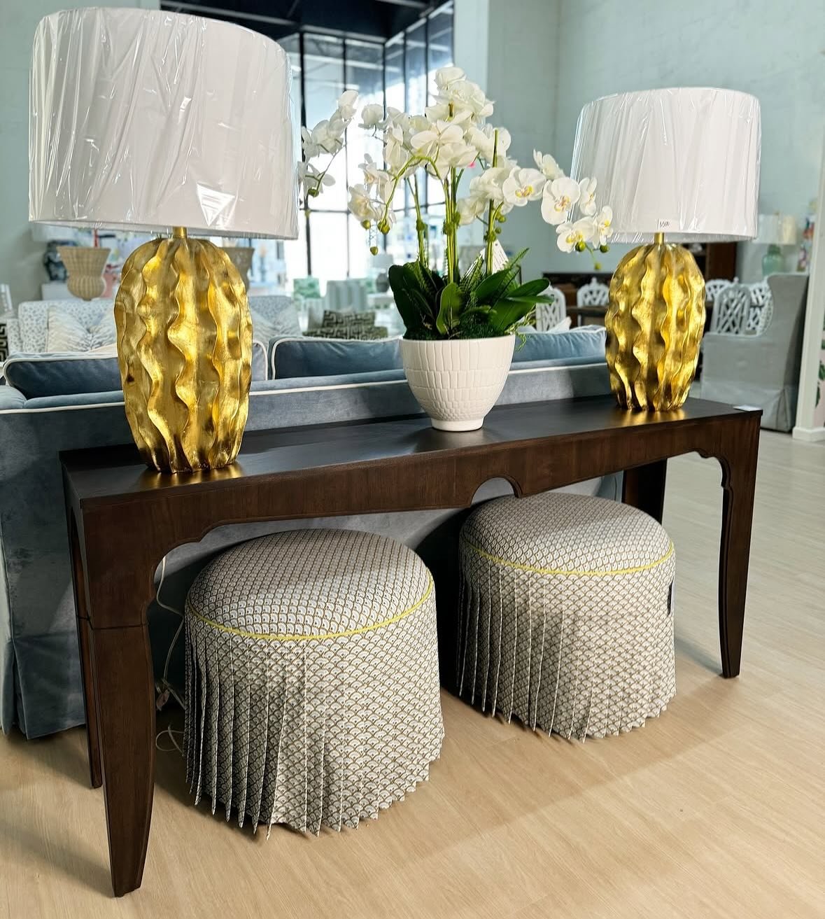 Dark wood console table with arched details and gold lamps behind a blue sofa