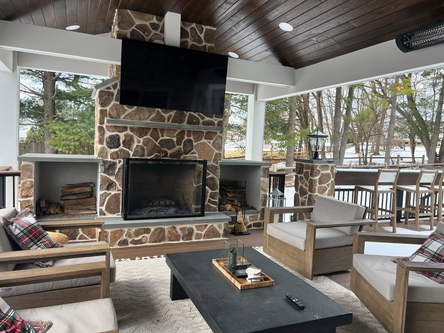 Rustic outdoor fireplace built from irregularly shaped brown and gray fieldstone with flanking square concrete log storage niches.
