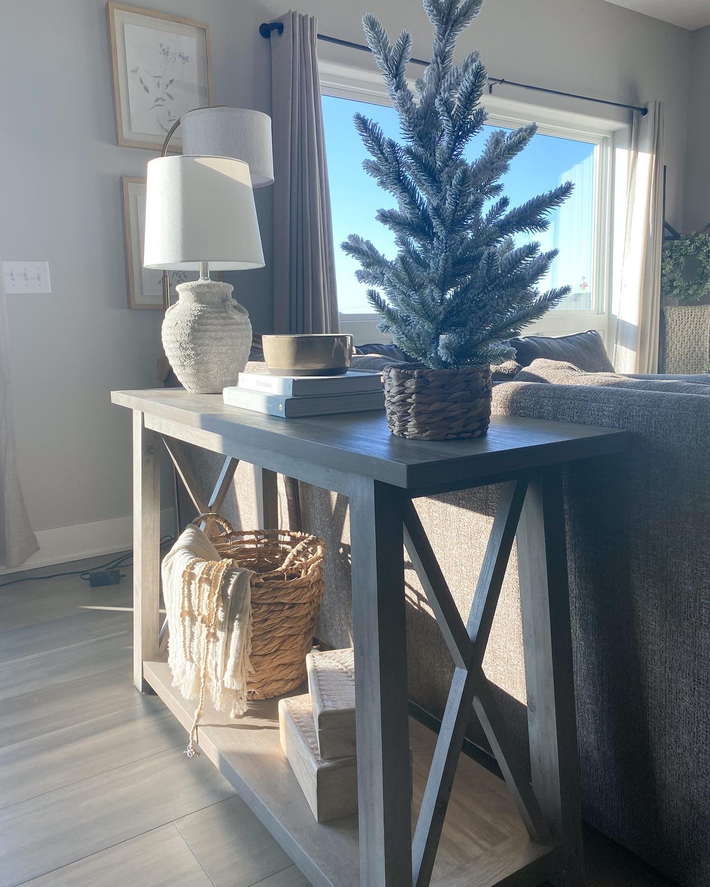 Grey wooden console table with X-sides styled with winter decor behind a sofa