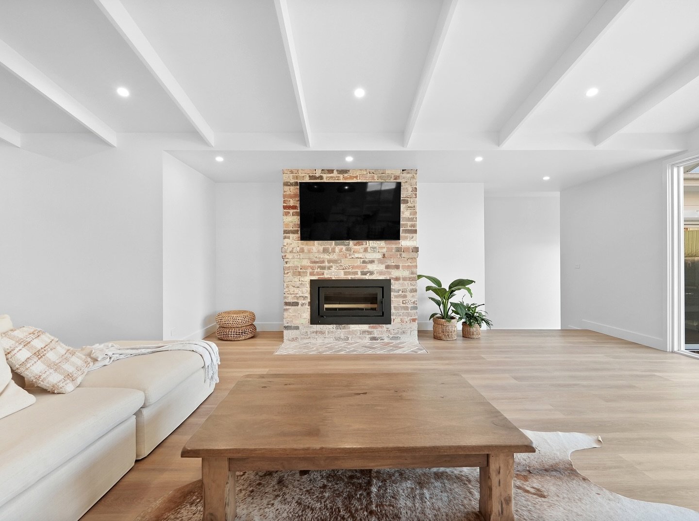 A contemporary living room with a floor-to-ceiling brick feature wall painted with a heavy whitewash. A flat black firebox is installed centrally in the brick.