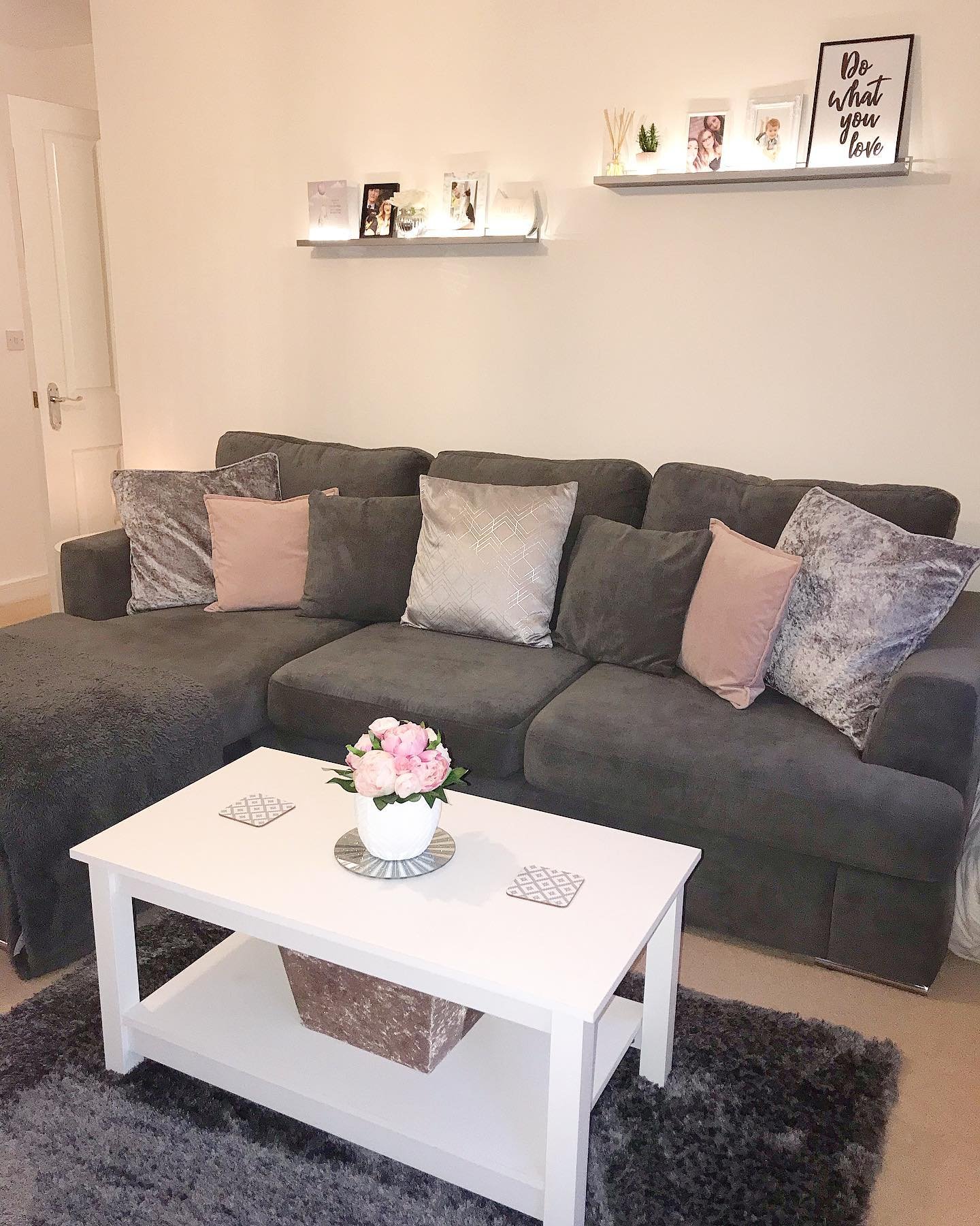 Two short grey floating shelves with lights and family photos above dark grey couch