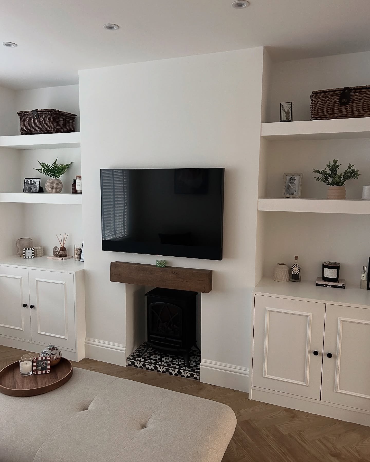 White built-in alcove shelves with wicker baskets and a floating beam mantel above a tiled hearth.