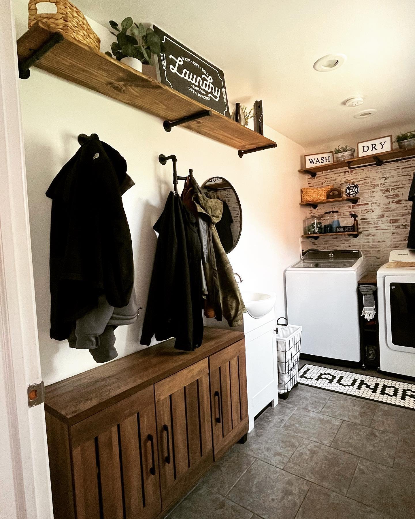 Wooden laundry shelves mounted on black industrial pipes above coat hooks and washing machines