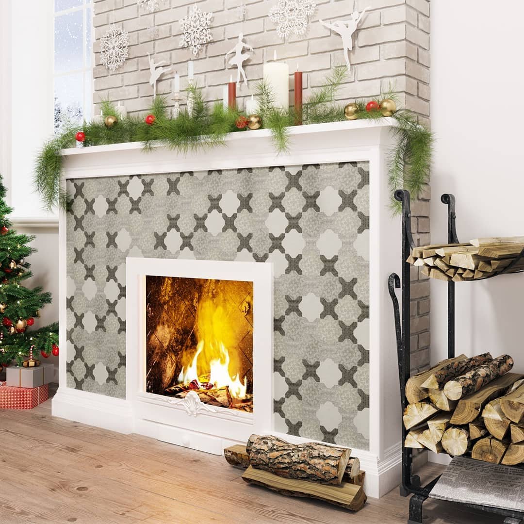 A holiday-decorated fireplace with a white wood surround and a surround tiled with large, gray and off-white patterned quatrefoil tiles.