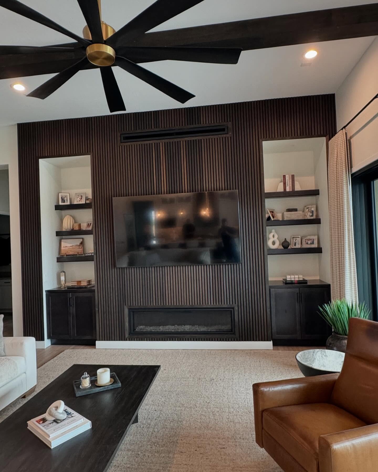 Contemporary living room featuring a fireplace media wall clad in dark stained wood slats, with a horizontal fireplace and built-in shelving on either side.