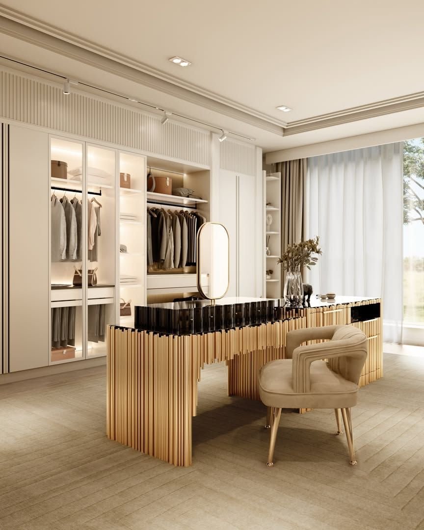 A luxury walk-in closet featuring a dramatic central island vanity desk with gold cylindrical piping, a tan velvet chair, and white illuminated wardrobes.